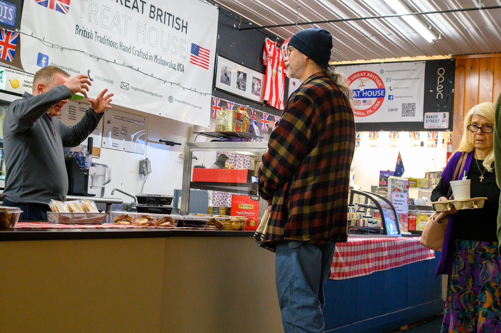People at a British food stall engaging with the vendor, with signs and flags indicating British products and decor.