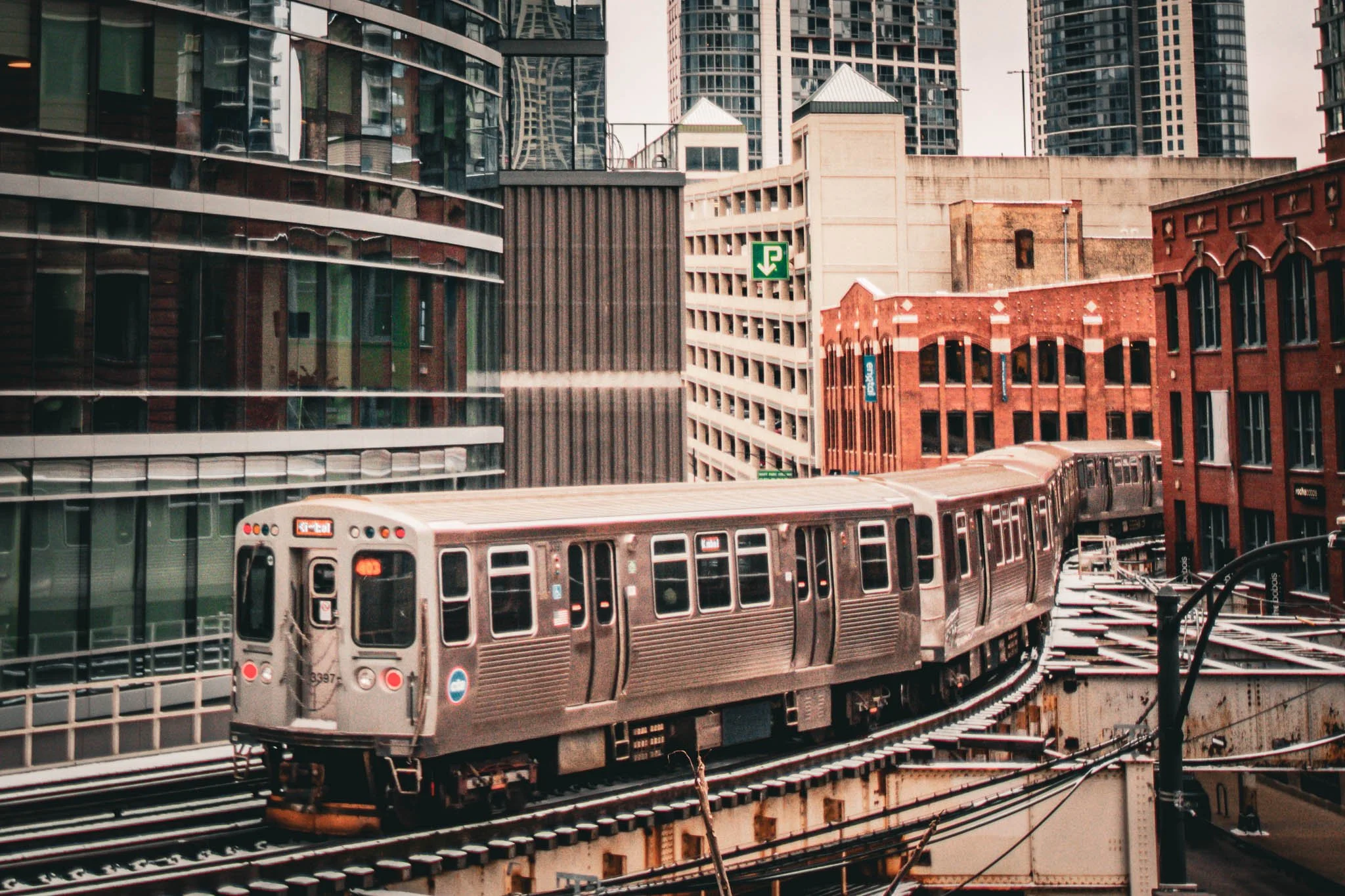 An urban train travels on elevated tracks through a city with modern and historic high-rise buildings.