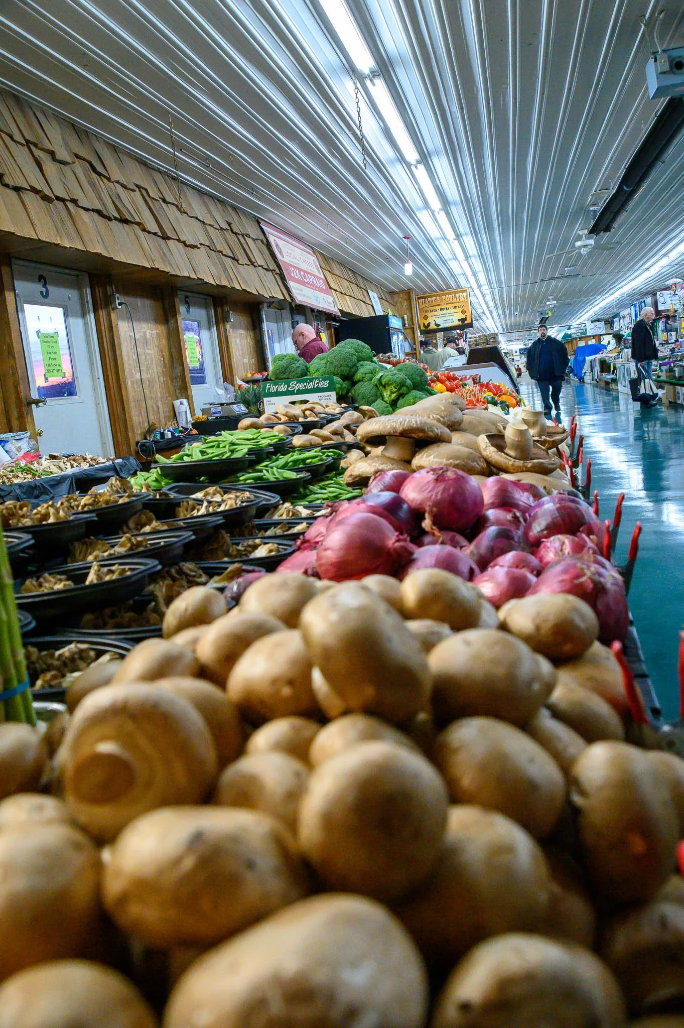 Fresh vegetables such as onions, mushrooms, broccoli, and celery displayed on a market stall inside a store aisle.