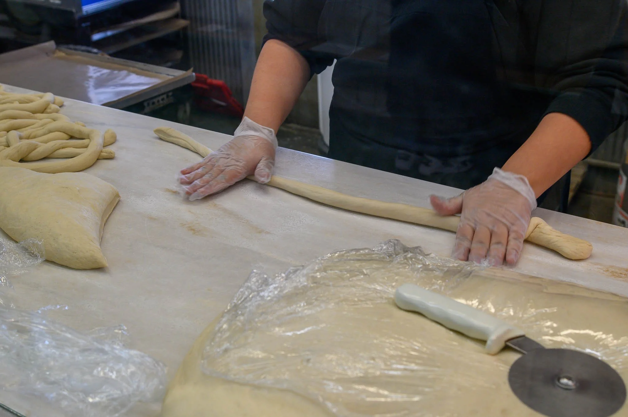 Person wearing gloves rolling out dough into long strands on a countertop.