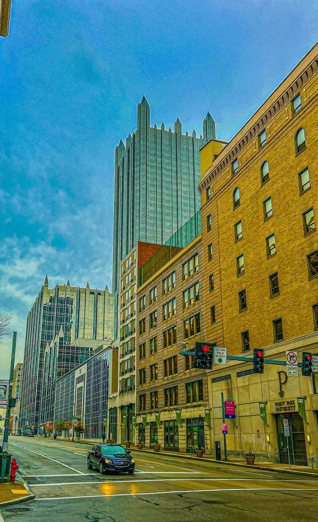 City street with tall skyscrapers, a black car on the road, traffic lights, and commercial buildings in downtown.