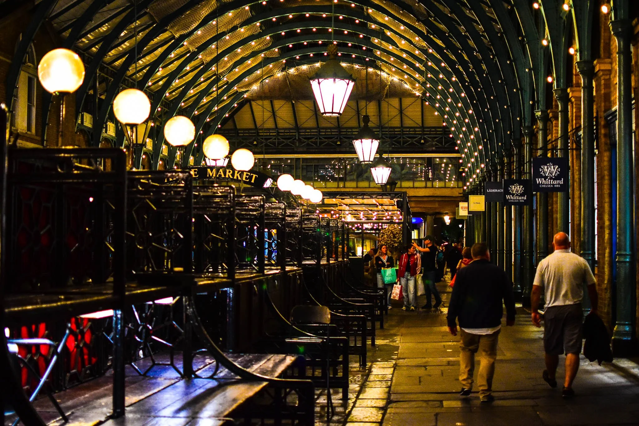 People walking under a decorated, illuminated archway at night outside a marketplace
