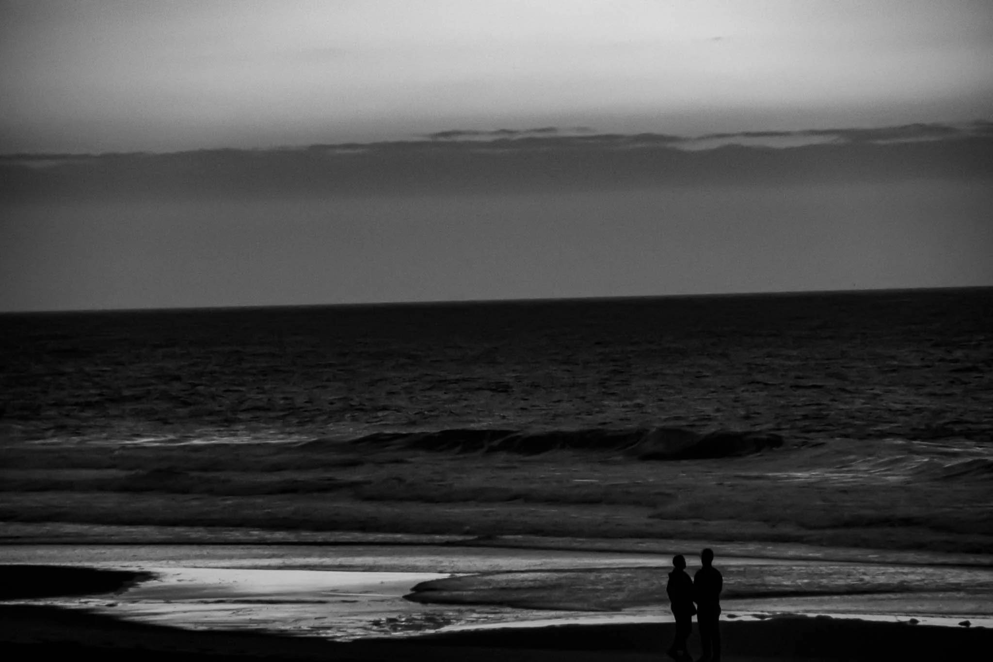 Silhouettes of two people standing on a beach at sunrise with waves in the background