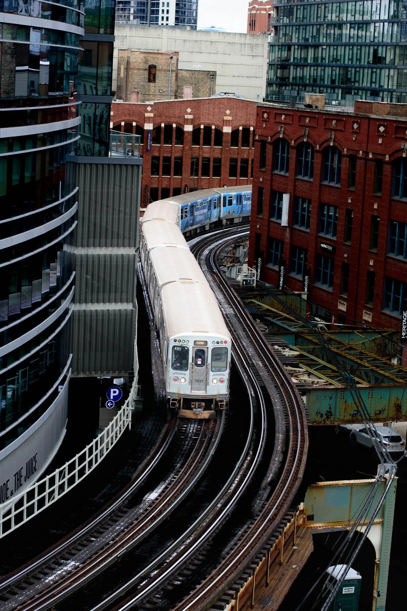 A train traveling on elevated tracks through a city with modern and historic buildings surrounding it.