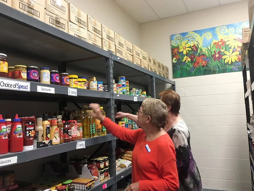 Two volunteer ladies putting food on a shelf