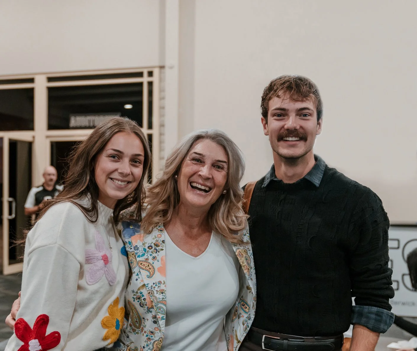 Three happy people with big smiles in the foyer. One lady in her sixties. One man and lady in their twenties.