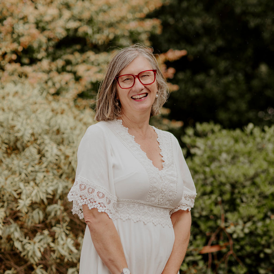 Sue is in her fifties wearing a white dress and red glasses