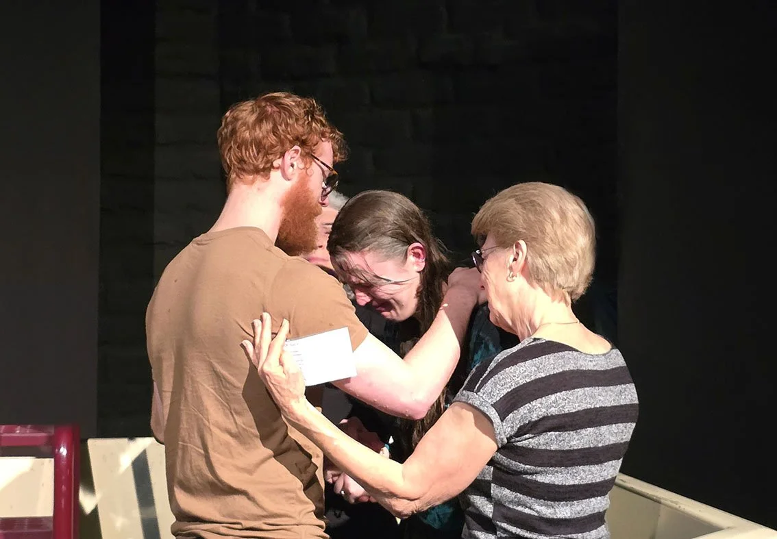 Man in his twenties and a lady in her sixties praying for a young lady in the baptstry