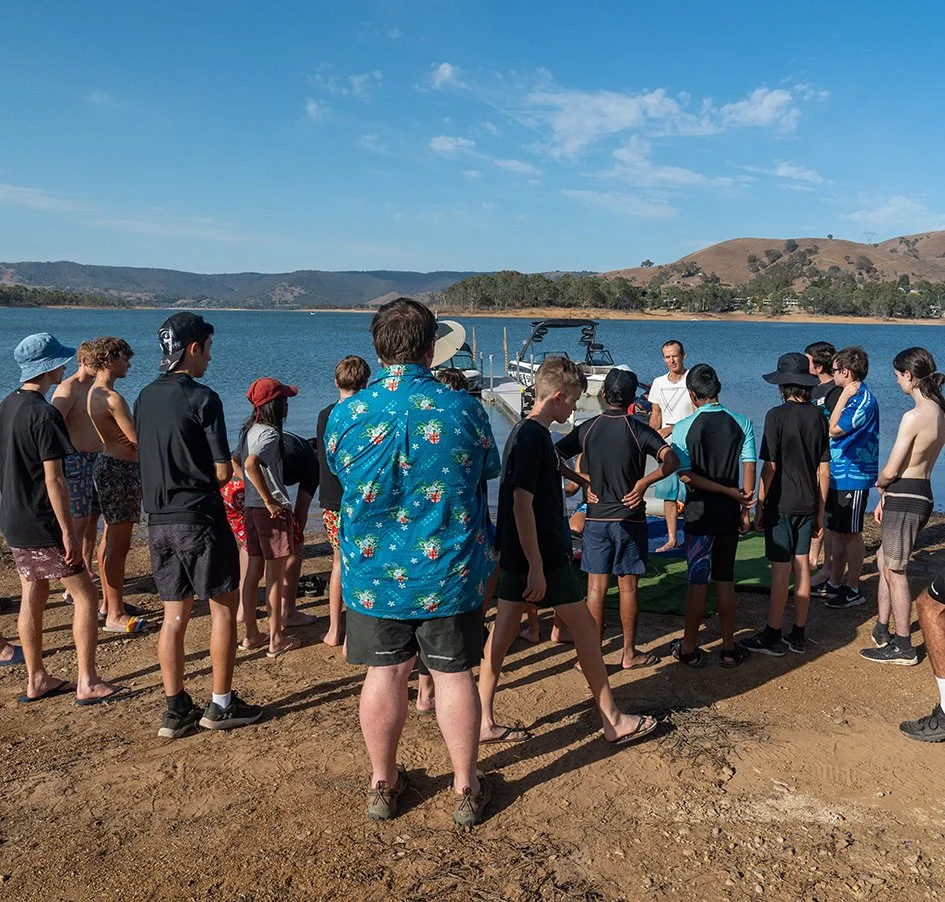 Boys in sports wear standing at the lakes edge near a boat