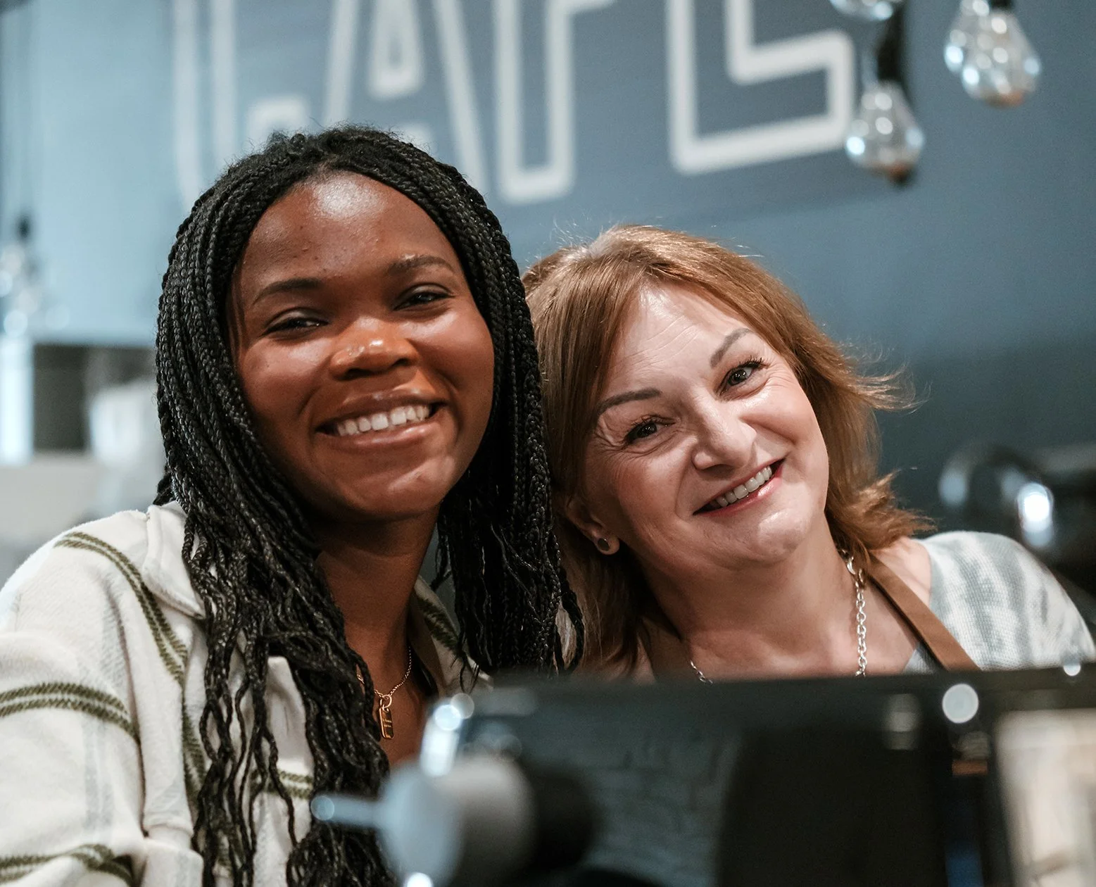Two women smiling and taking a selfie together in a room with blurred background.