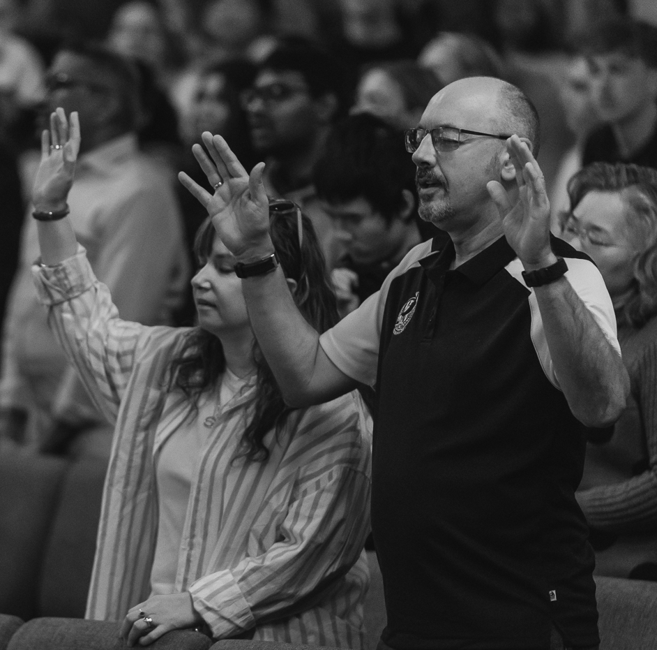 People with eyes closed and hands raised, engaged in prayer or worship in a church or religious gathering.