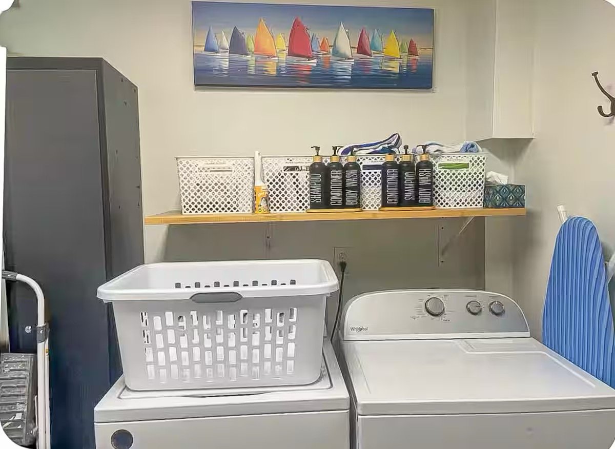 A laundry room with a washing machine, a laundry basket, and shelves holding laundry supplies and decorative items.