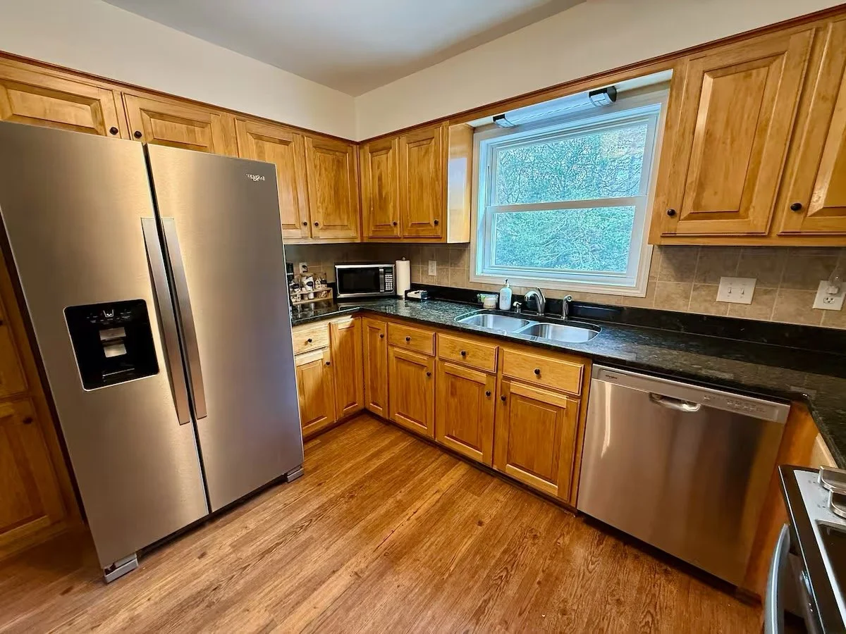 Kitchen with wooden cabinets, stainless steel refrigerator, microwave, dishwasher, and a window above the sink.