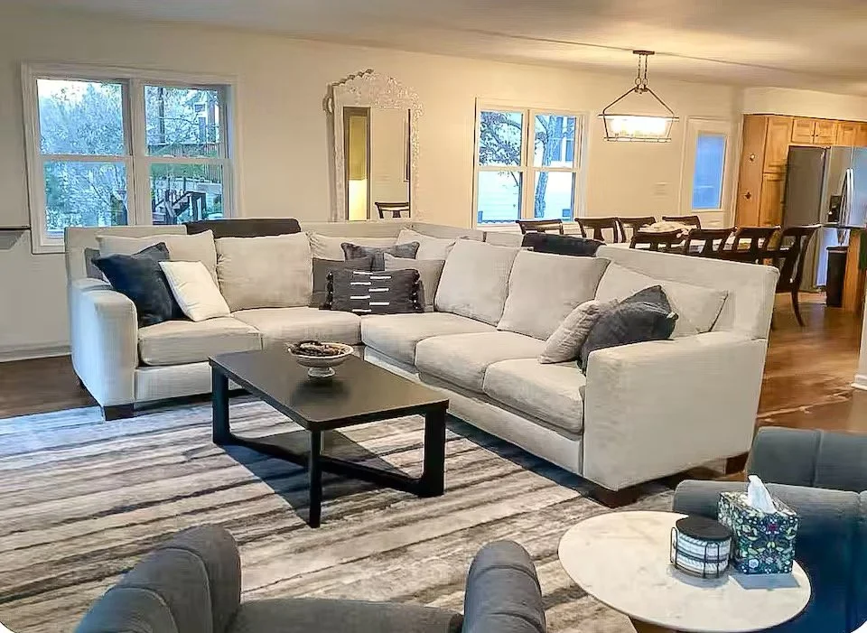 Living room with a large sectional sofa, decorative pillows, a coffee table, and windows showing an outdoor scene.