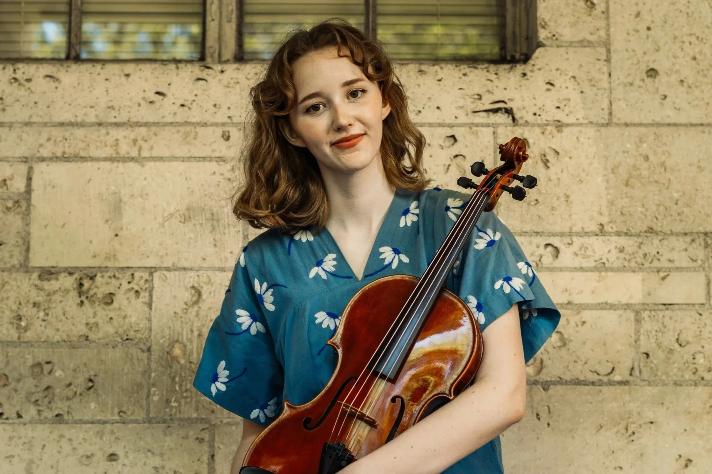 Ella holds her viola in a blue dress painted with daisies. Photo taken by Tyler Pena