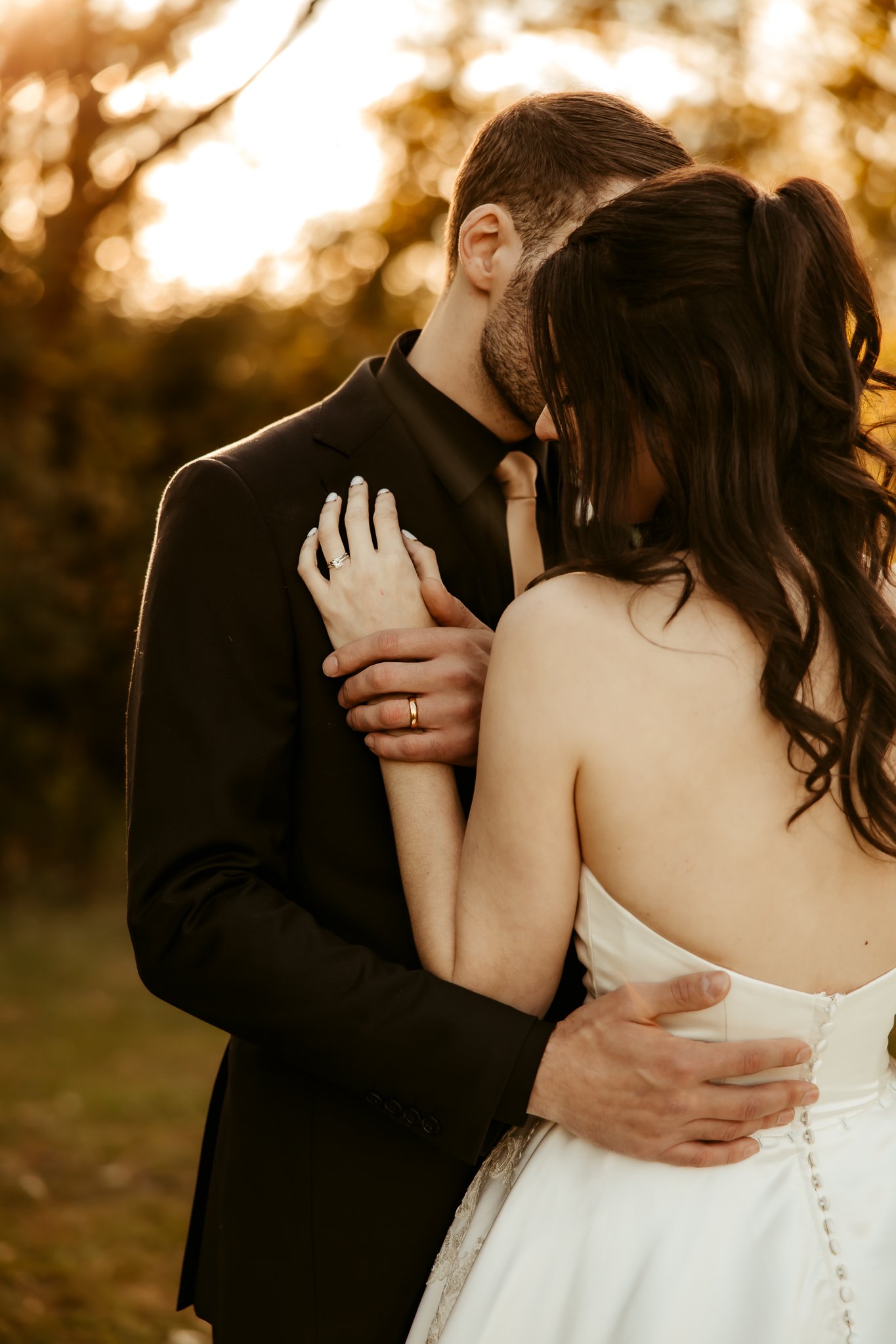 A couple embracing outdoors at sunset, with the woman in a wedding dress and the man in a suit, holding each other close. Minnesota wedding photography 