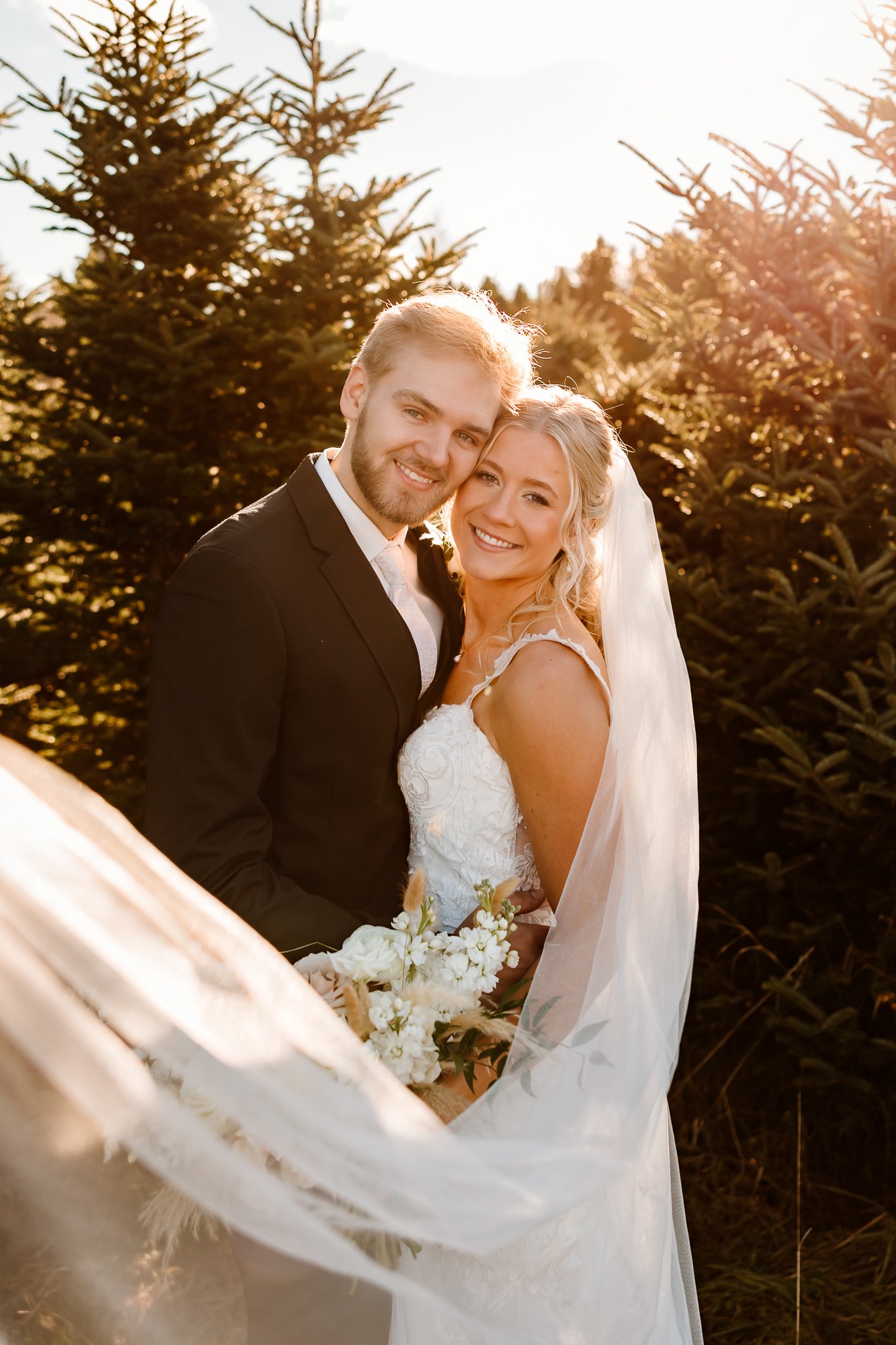 A happy bride and groom embracing outdoors during sunset, with trees in the background.