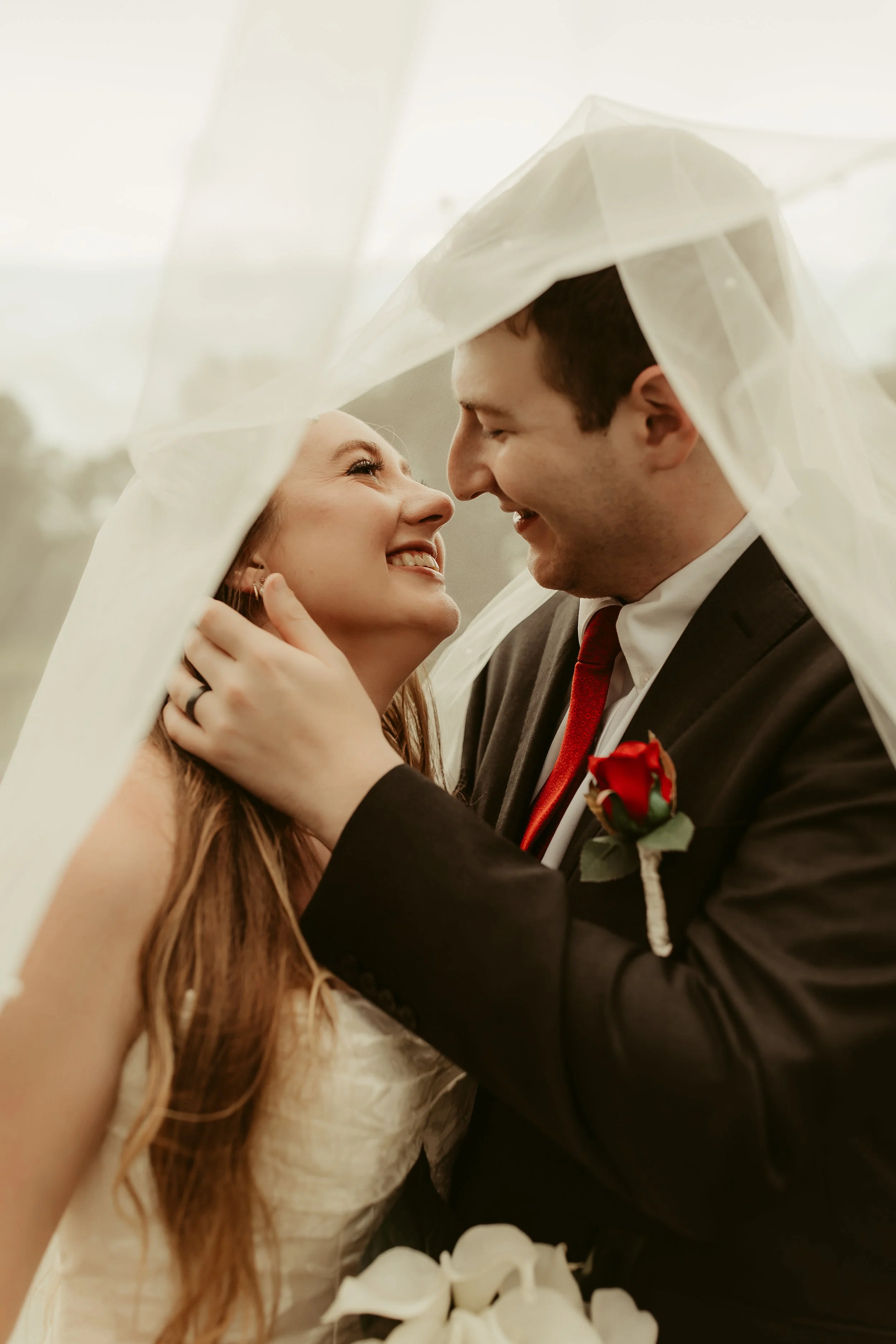 A newly married couple smiling and gazing into each other's eyes under a veil.