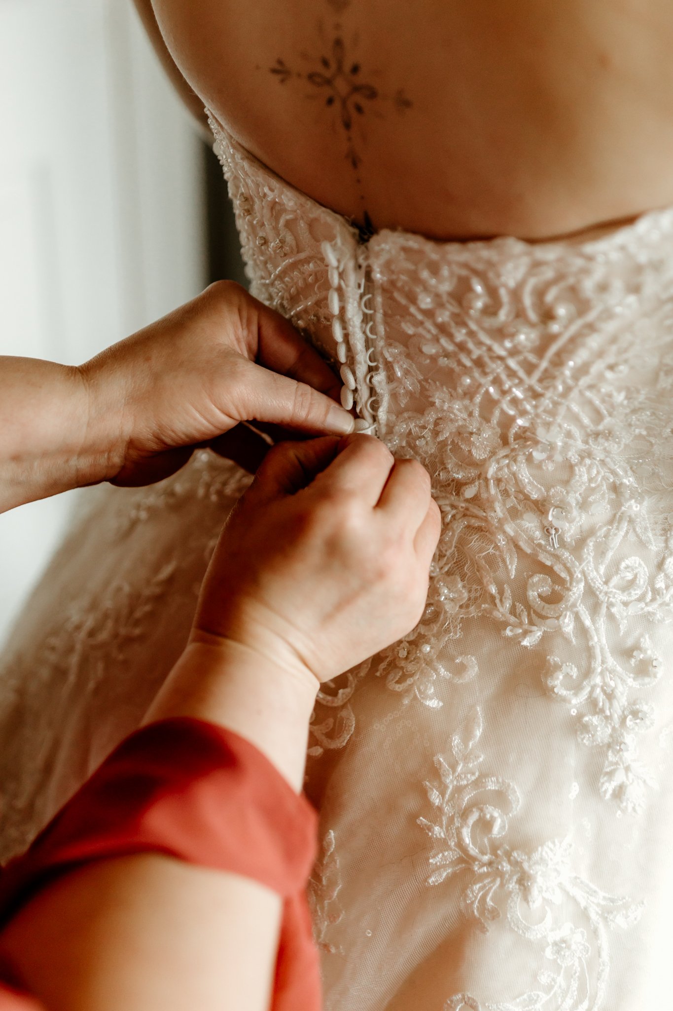 Close-up of hands fastening buttons on the back of a wedding dress with intricate lace embroidery.