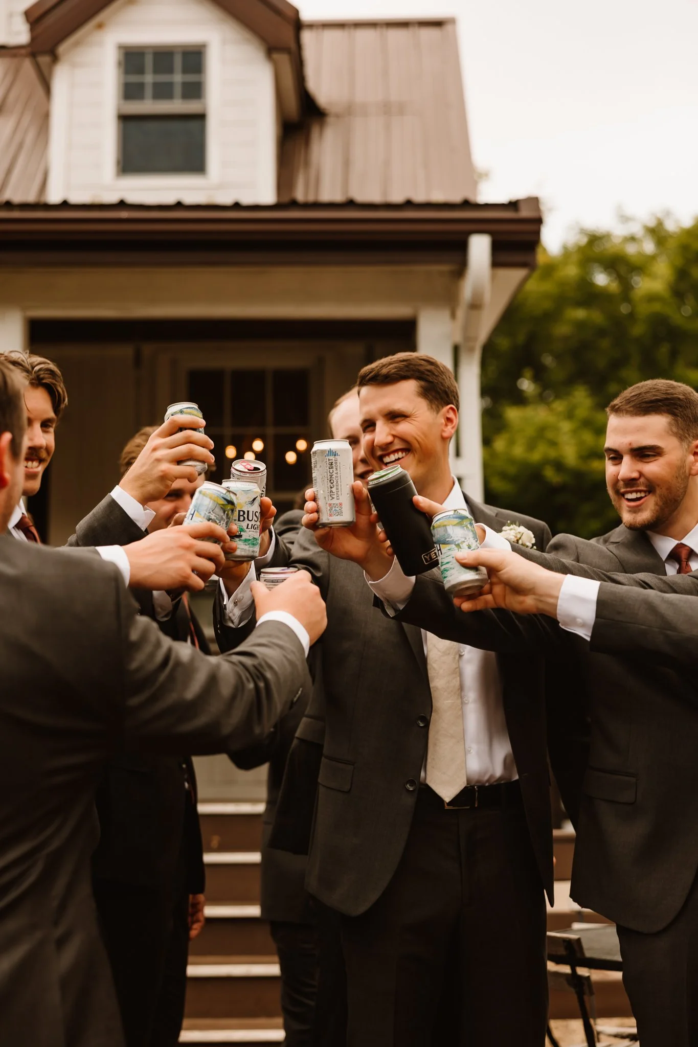 Group of men in suits raising cans for a toast outside a house
