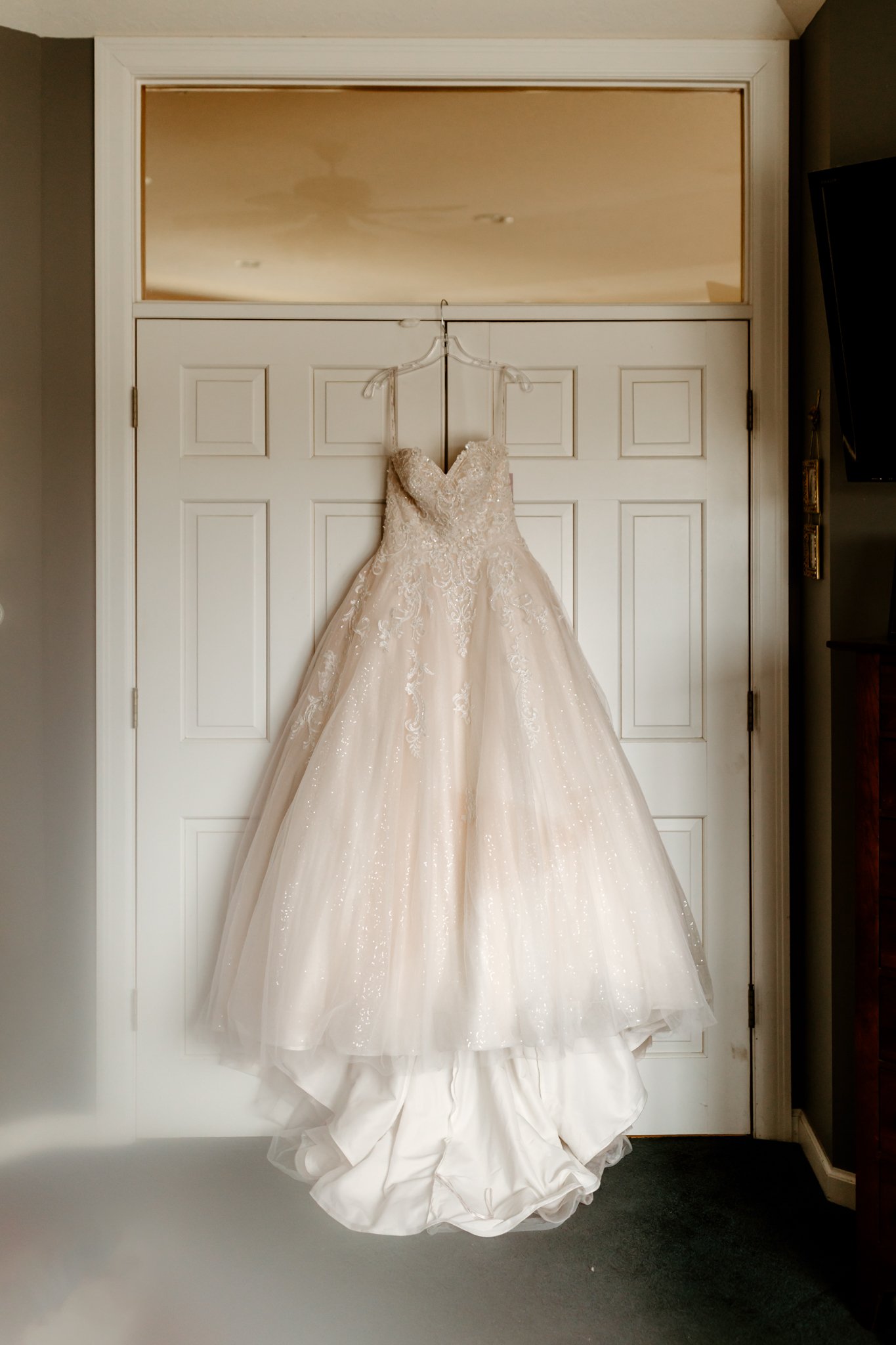 A wedding dress hanging on a hanger on a white door with a glass panel above.