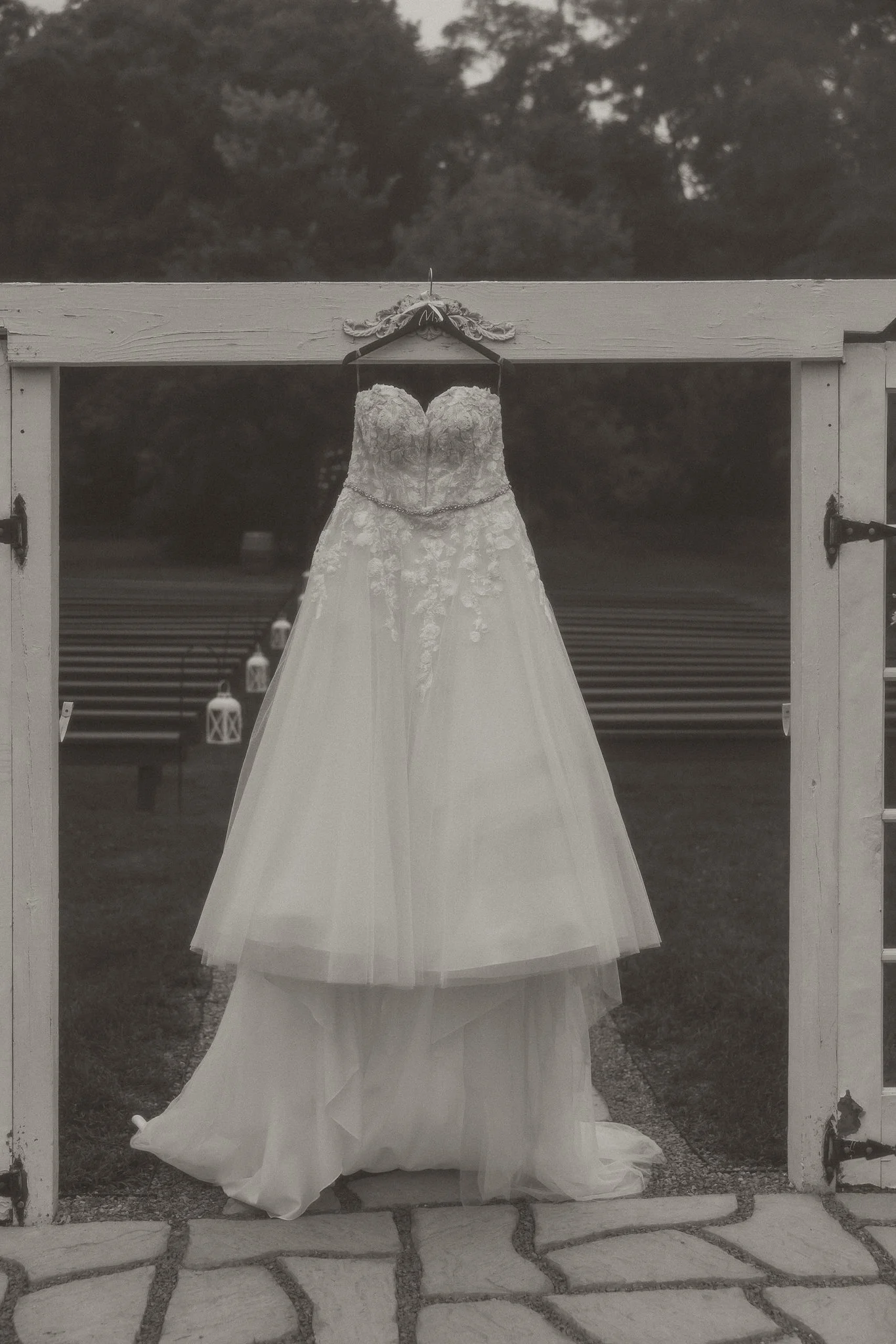 A wedding dress hanging on a barn door with lanterns in the background.