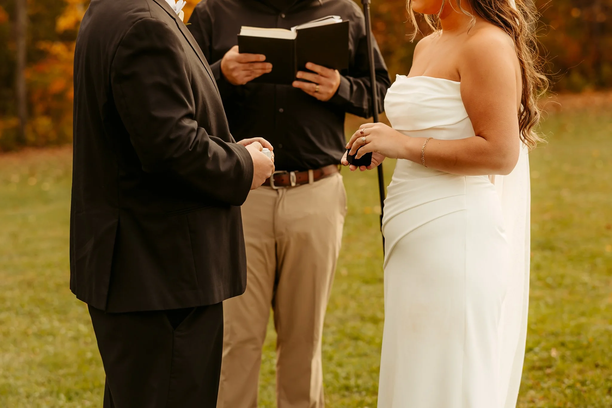 A couple getting married outdoors, standing face-to-face, with a person officiating and holding a book.