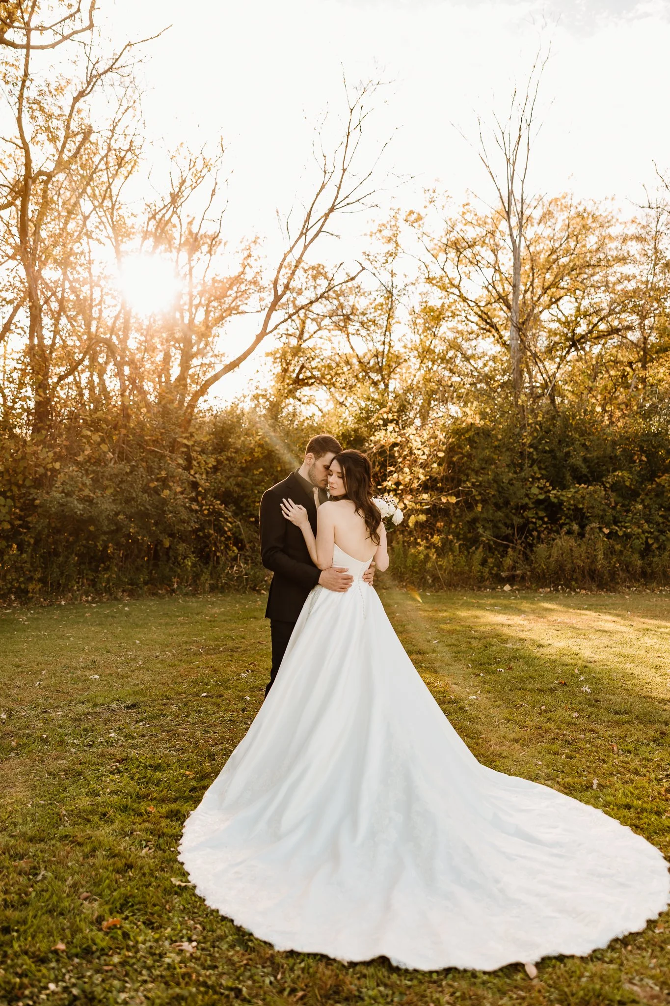 A bride and groom embrace outdoors during sunset, with trees and sunlight in the background. Harris Minnesota 