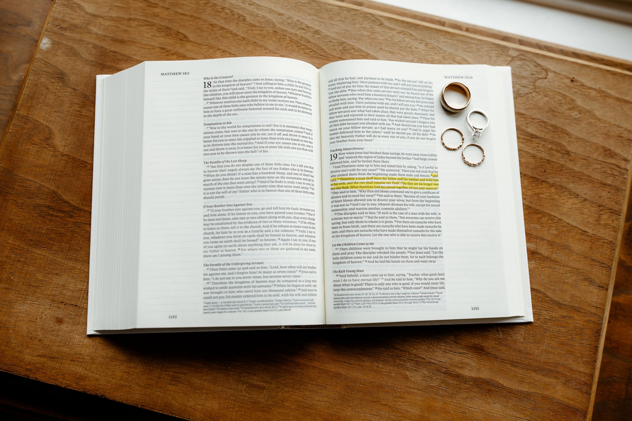 Open Bible on a wooden table with four rings placed on the top right page.