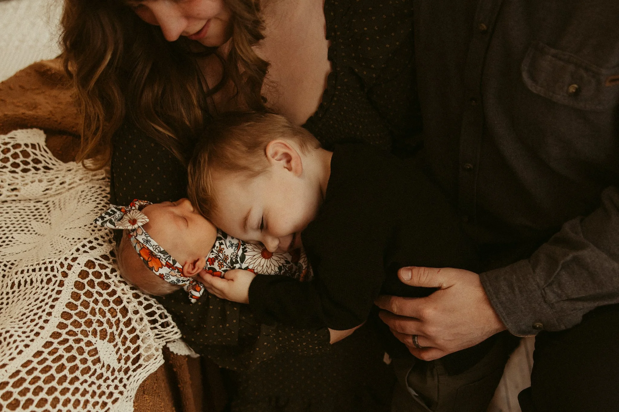 A family of four, including a newborn, a young boy, a woman, and a man, all hugging together and smiling.