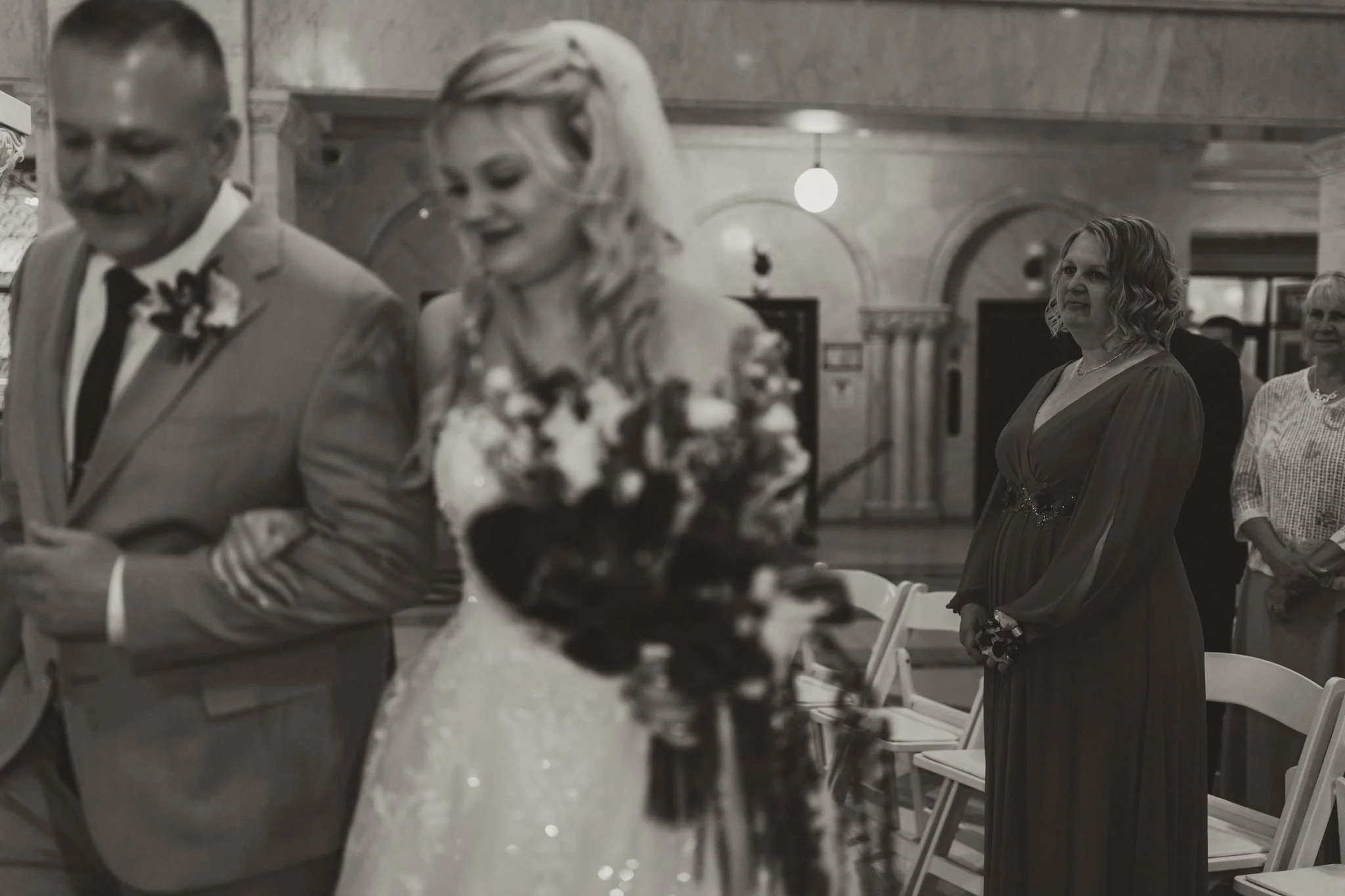A bride and groom are walking down the aisle as guests look on during a wedding ceremony in an ornate indoor venue.