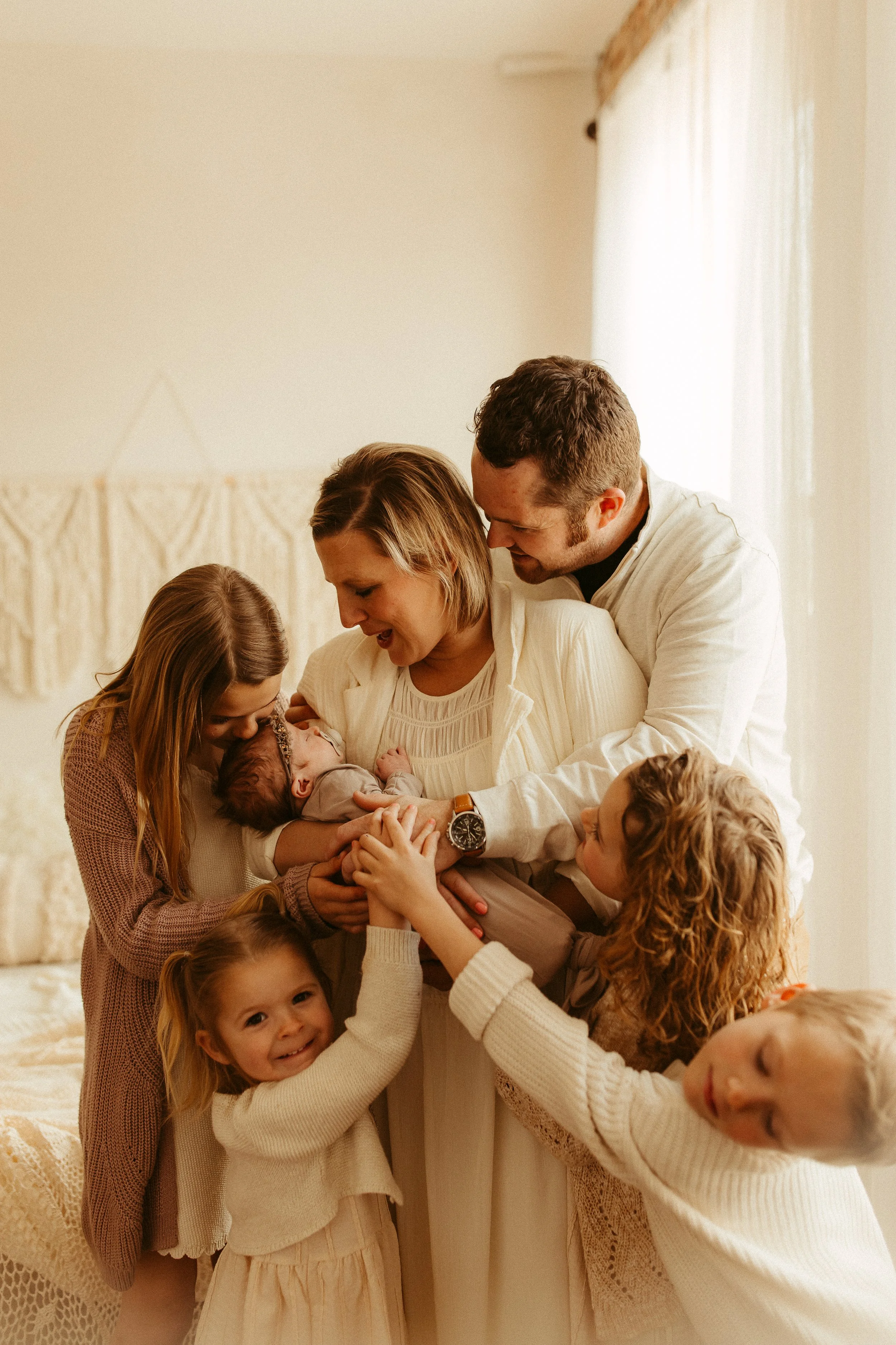 Family of eight holding a newborn baby together in a cozy room with beige decor and soft natural lighting.