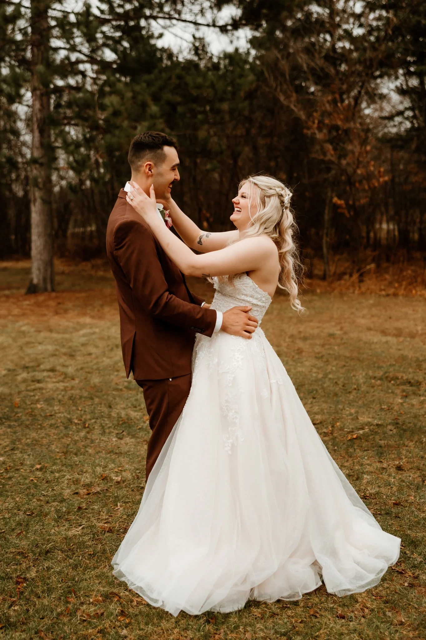 A bride and groom are embracing outdoors on their wedding day, with trees in the background.