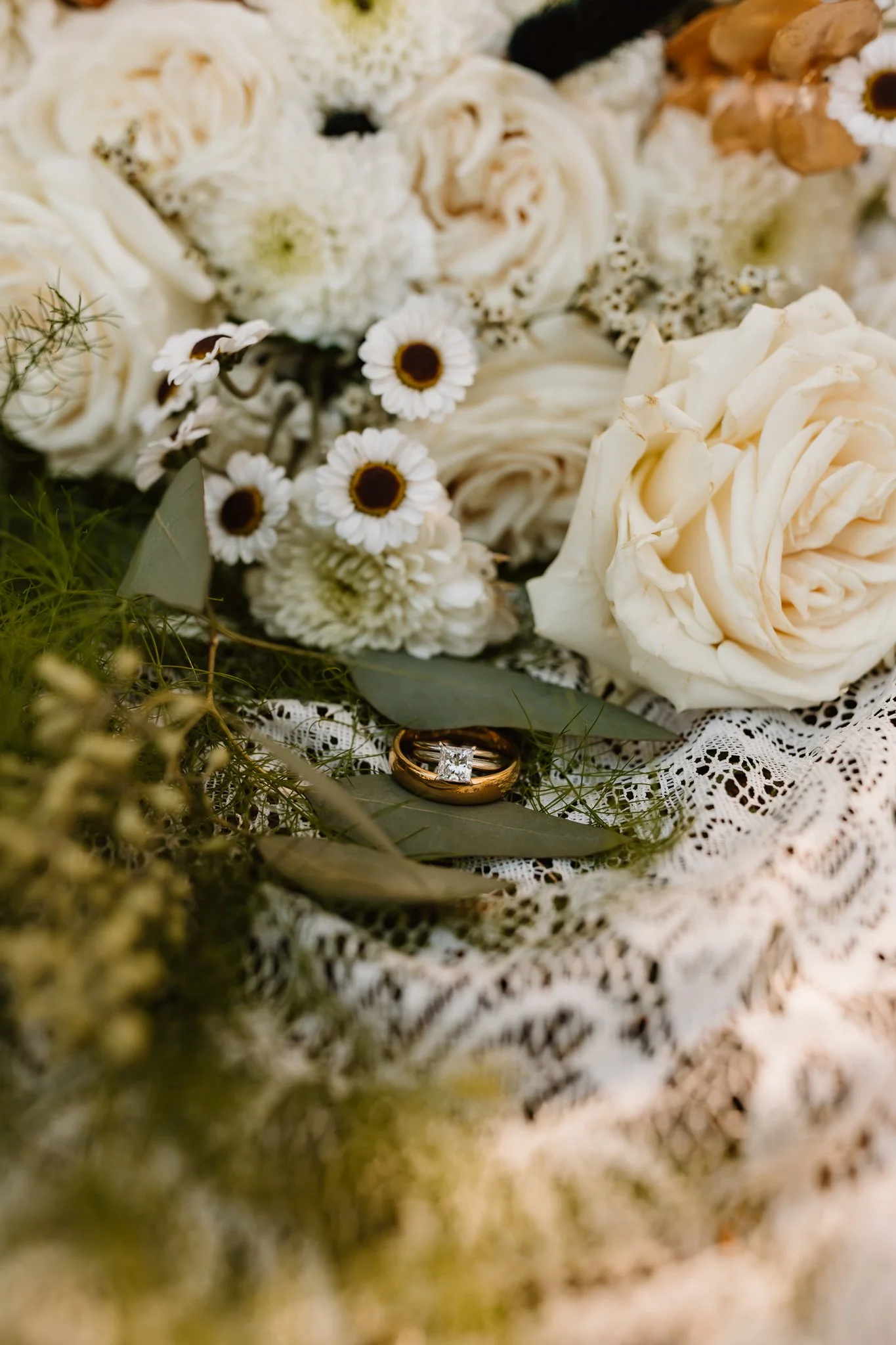 A bouquet of white flowers with wedding rings placed on a lace cloth.
