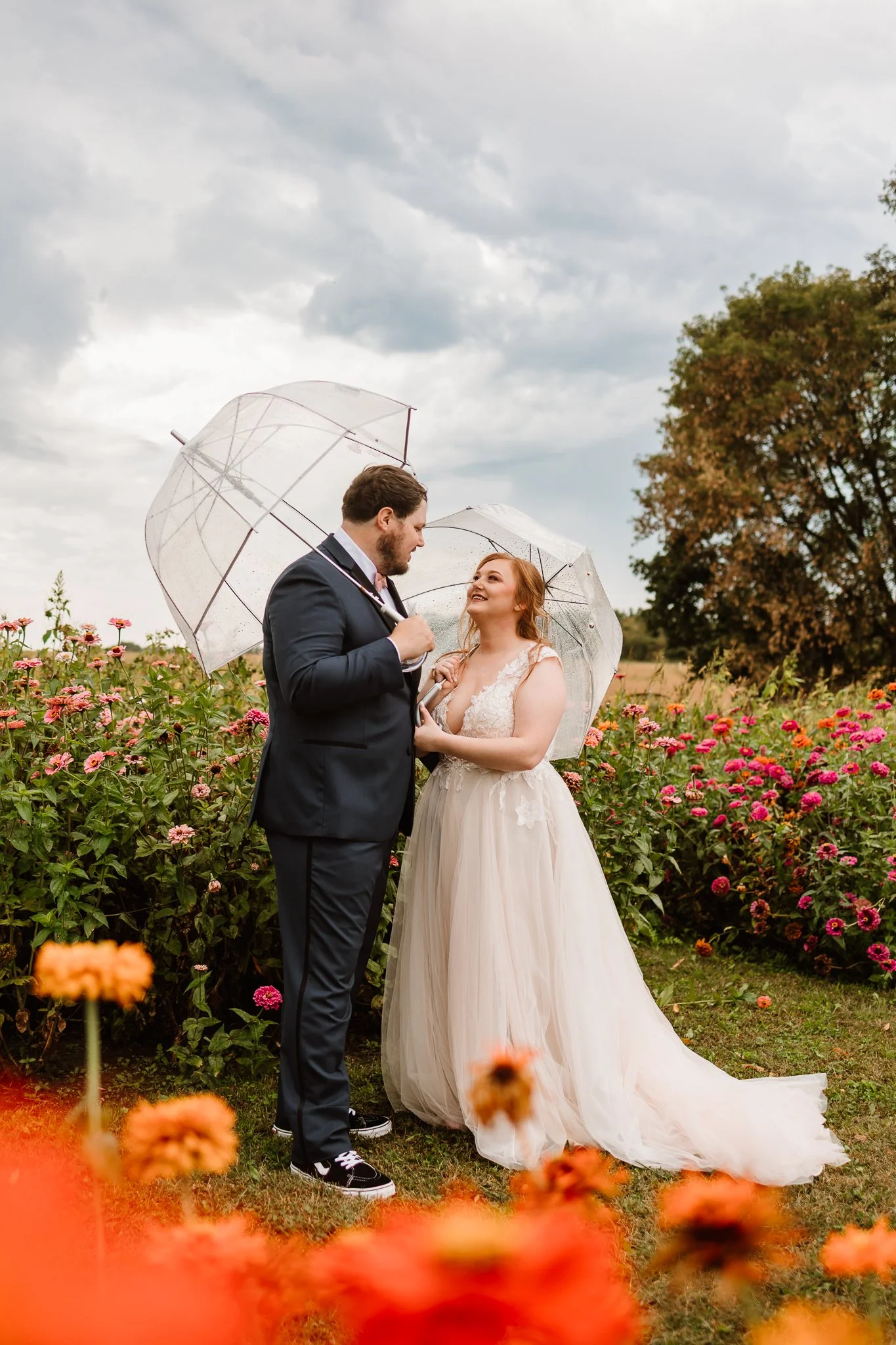 A bride and groom standing in a flower garden holding umbrellas on a cloudy day.Cambridge Pine city Minnesota Wedding