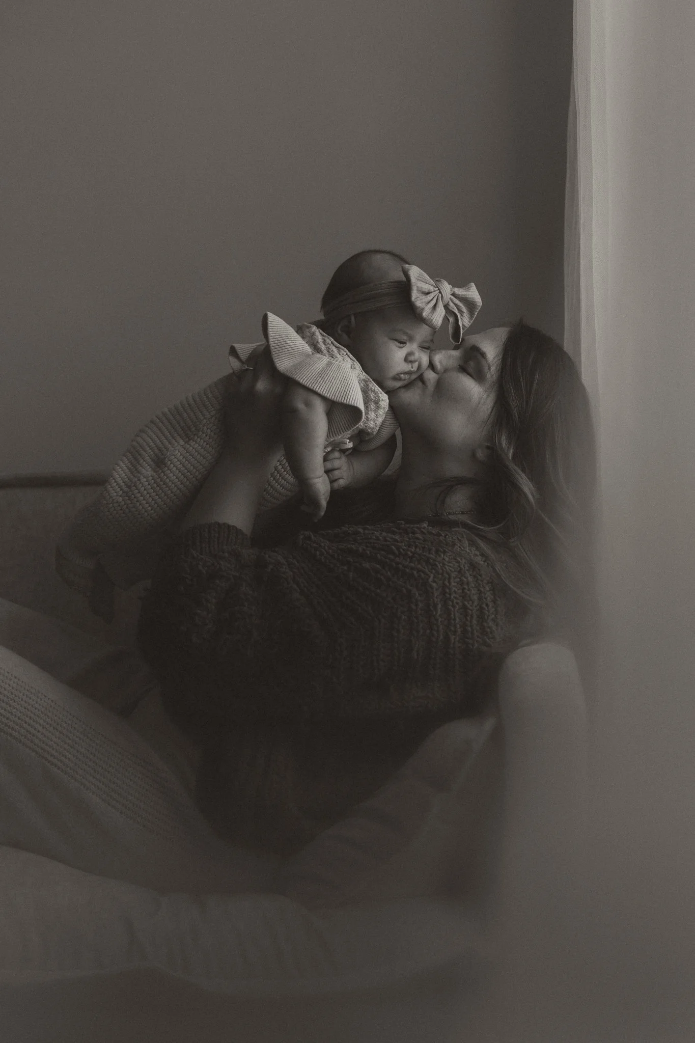 A woman holding a baby girl and giving her a kiss.