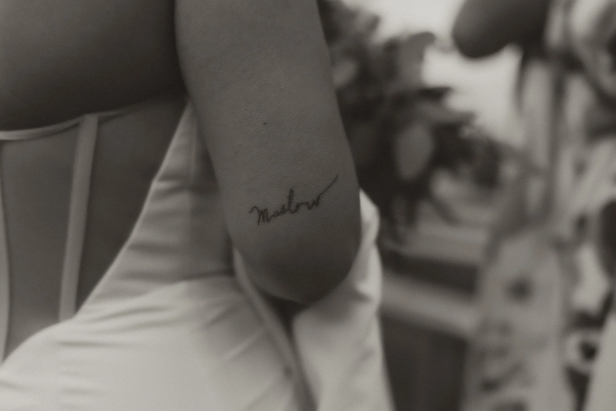 Close-up of a person's ankle with a tattoo of the name 'Marlow' in cursive script, with part of their leg and a white shirt visible.