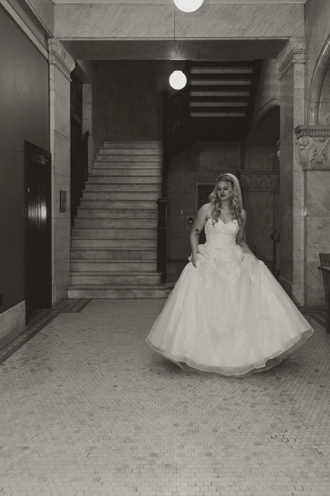 A woman in a wedding dress standing inside a building near a staircase.