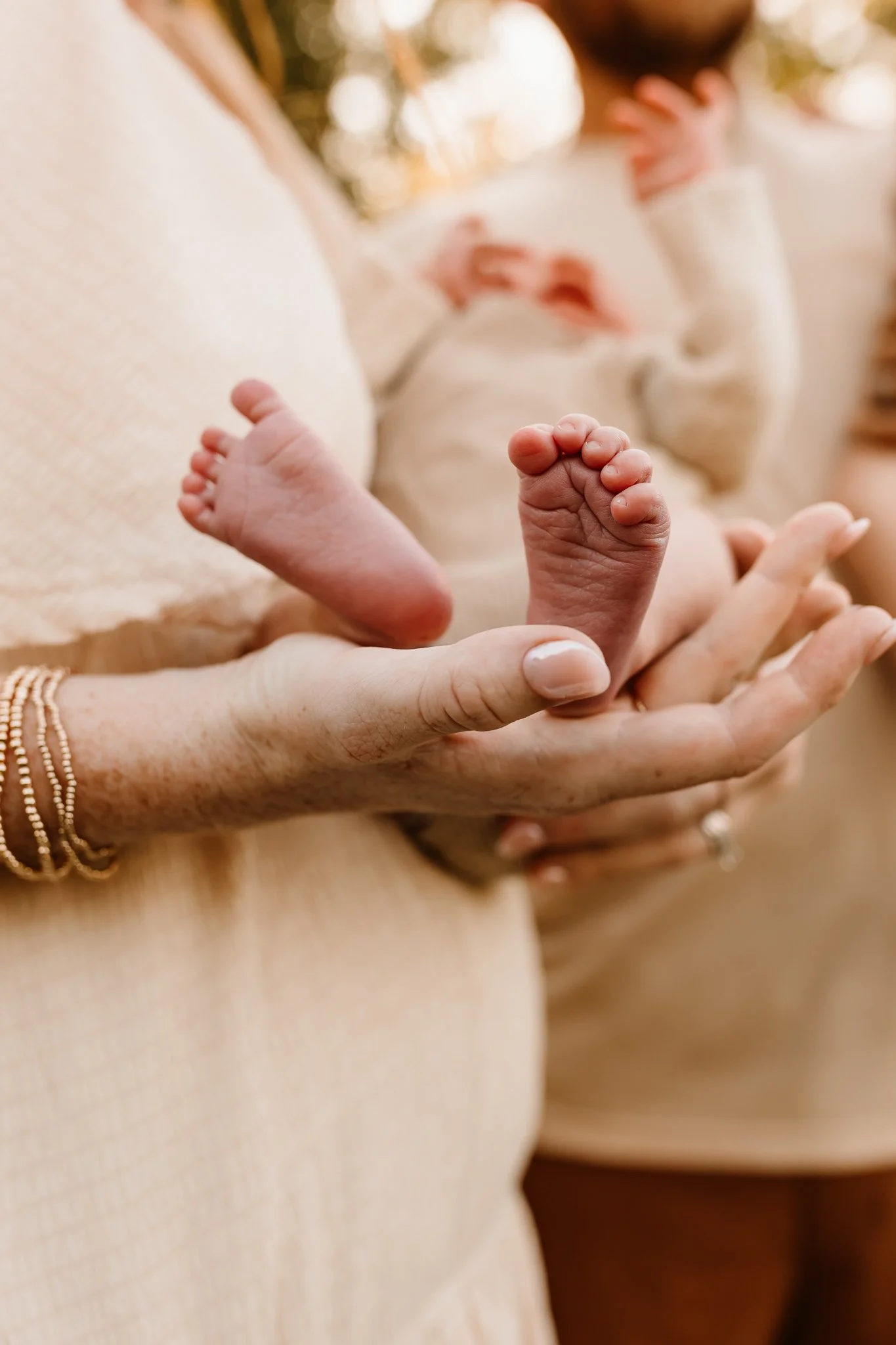 A person holding a tiny, newborn baby's foot in their hand, with other people holding baby's hands in the background.