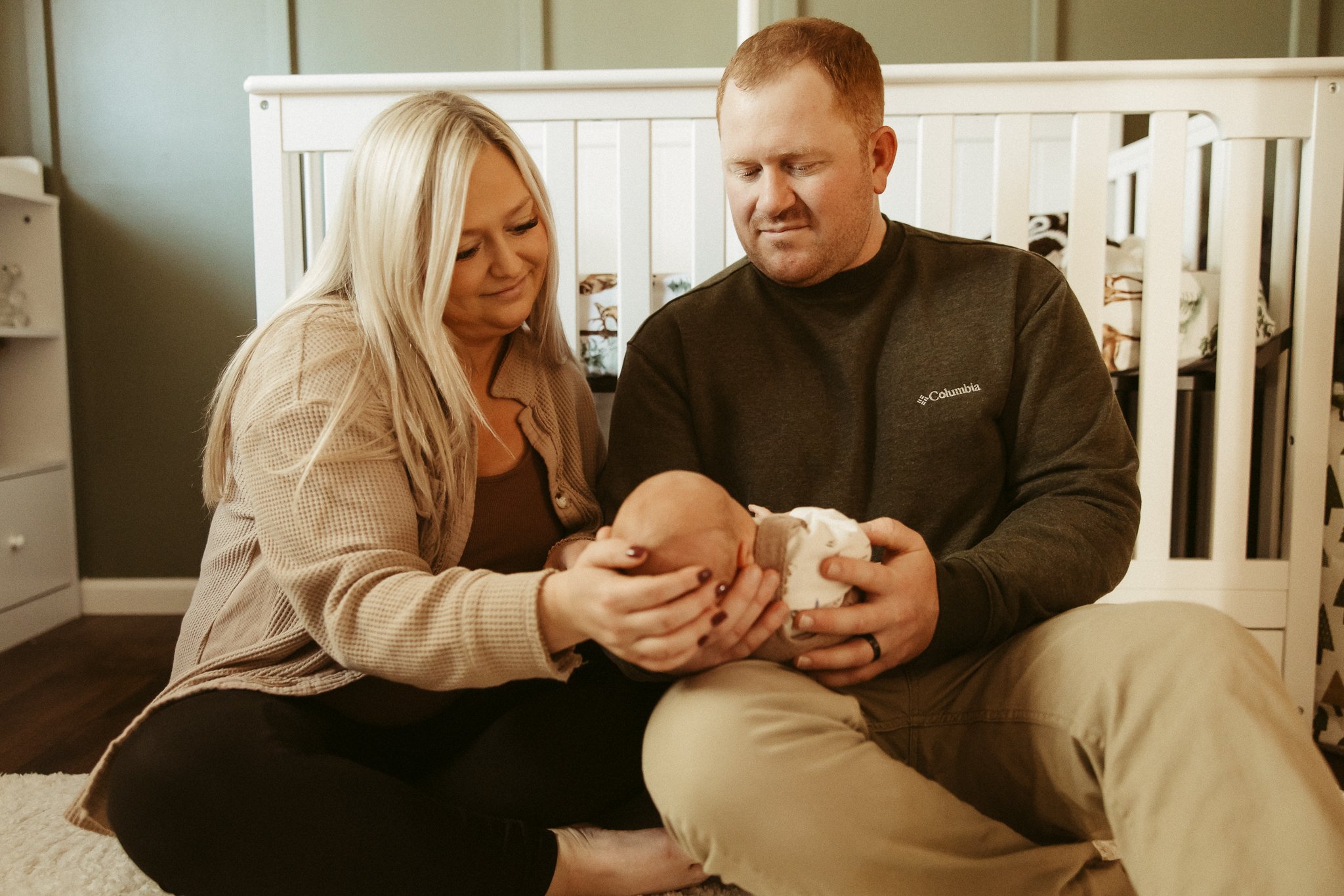 Couple holding their newborn baby in a nursery.