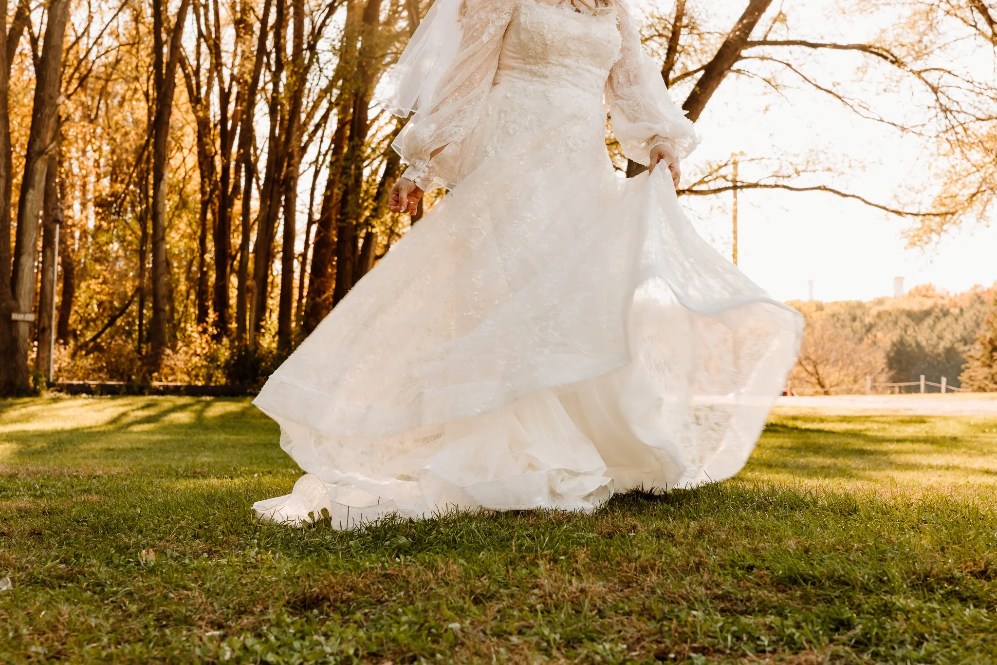 A bride in a white wedding gown walking on grass in a park during sunset.