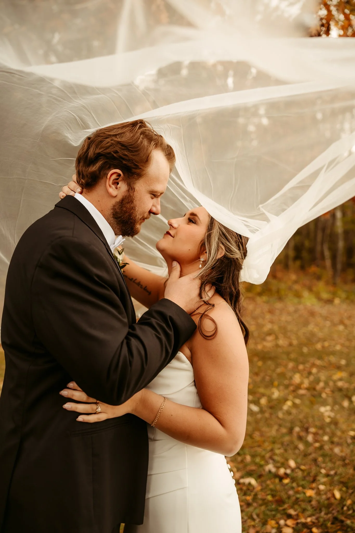 A bride and groom on their wedding day sharing a romantic moment outdoors, with the bride's veil floating around them.