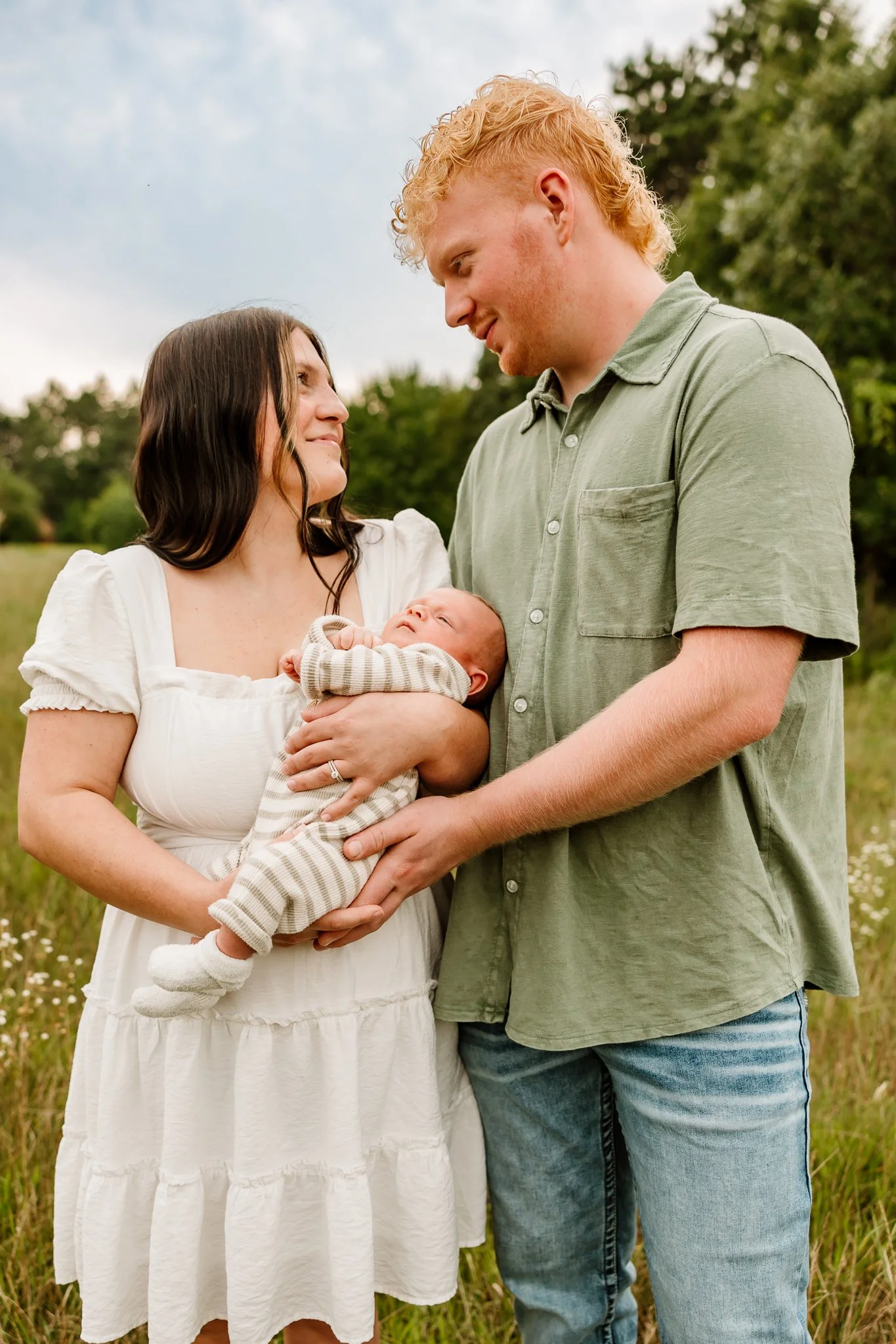 A family holding a newborn outdoors in a grassy field with trees in the background. North Branch Minnesota 