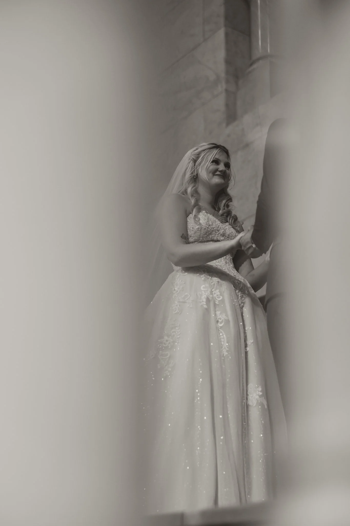 A bride and groom holding hands during their wedding ceremony, with the bride smiling and standing in a church or cathedral.