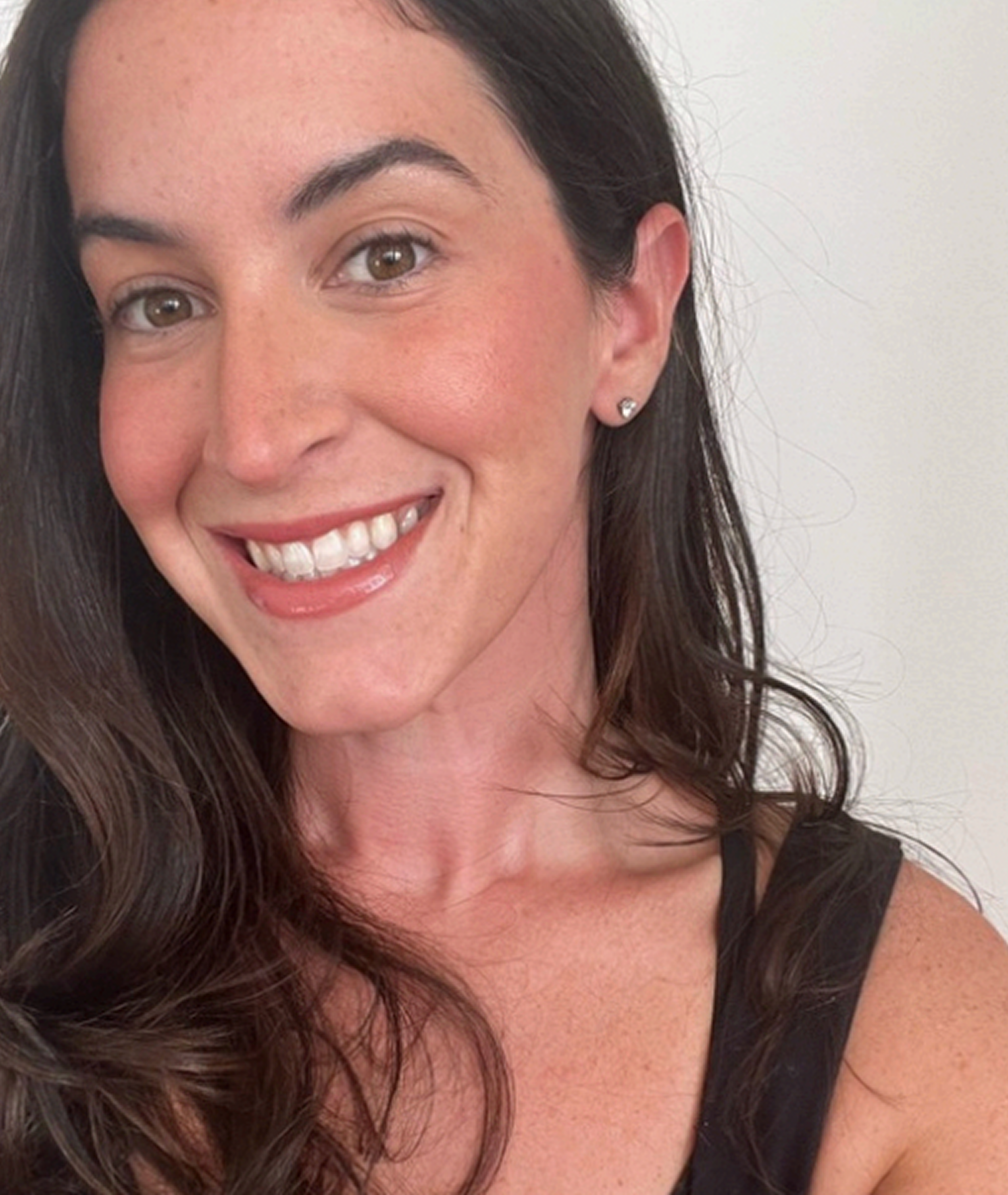 Close-up of a woman smiling with brown hair, earrings, and a black top.