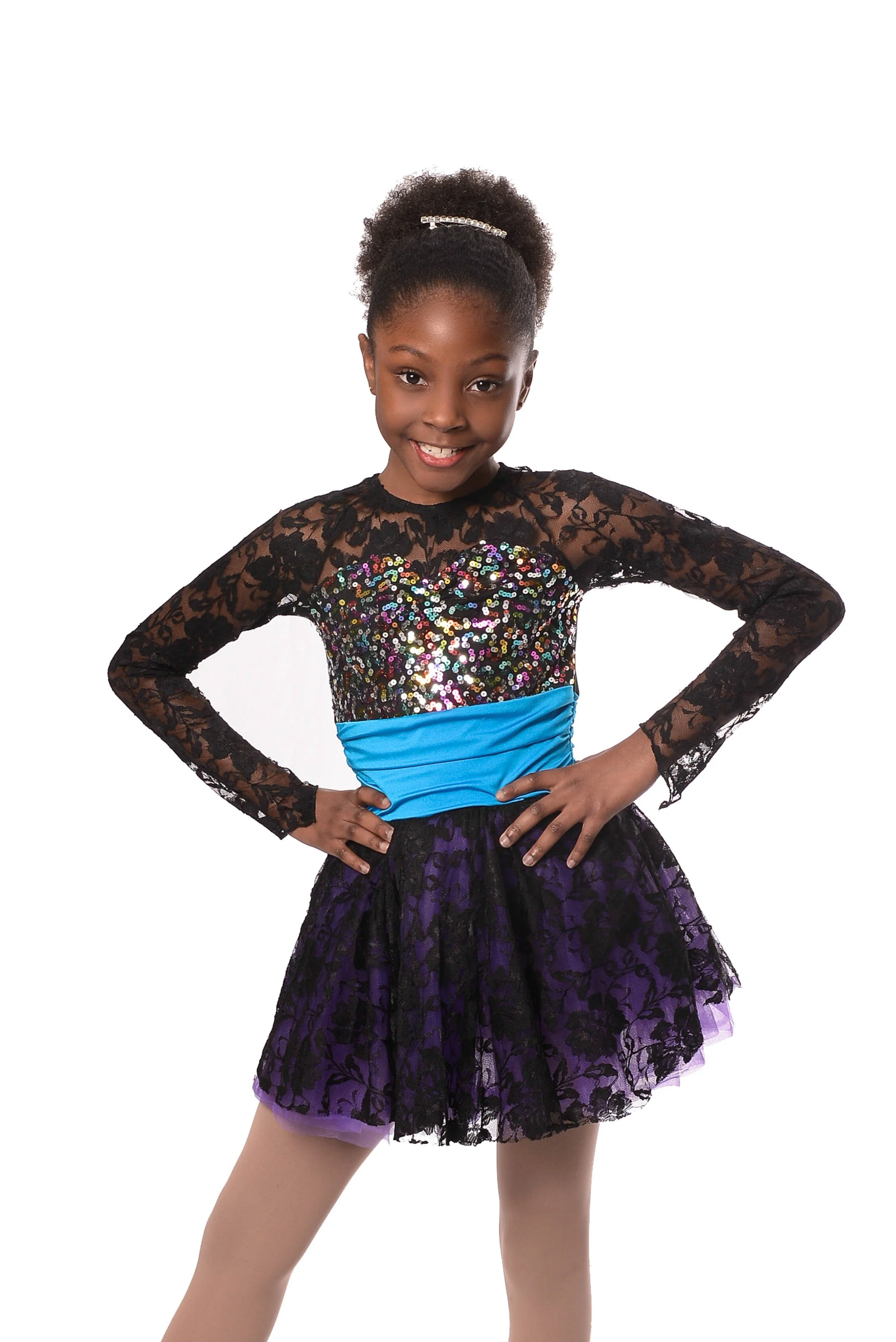 Professional dance photo of a young girl in colorful dress with black lace top, sequined bodice, blue waistband, and purple lace skirt, smiling with hands on hips, against a white background.