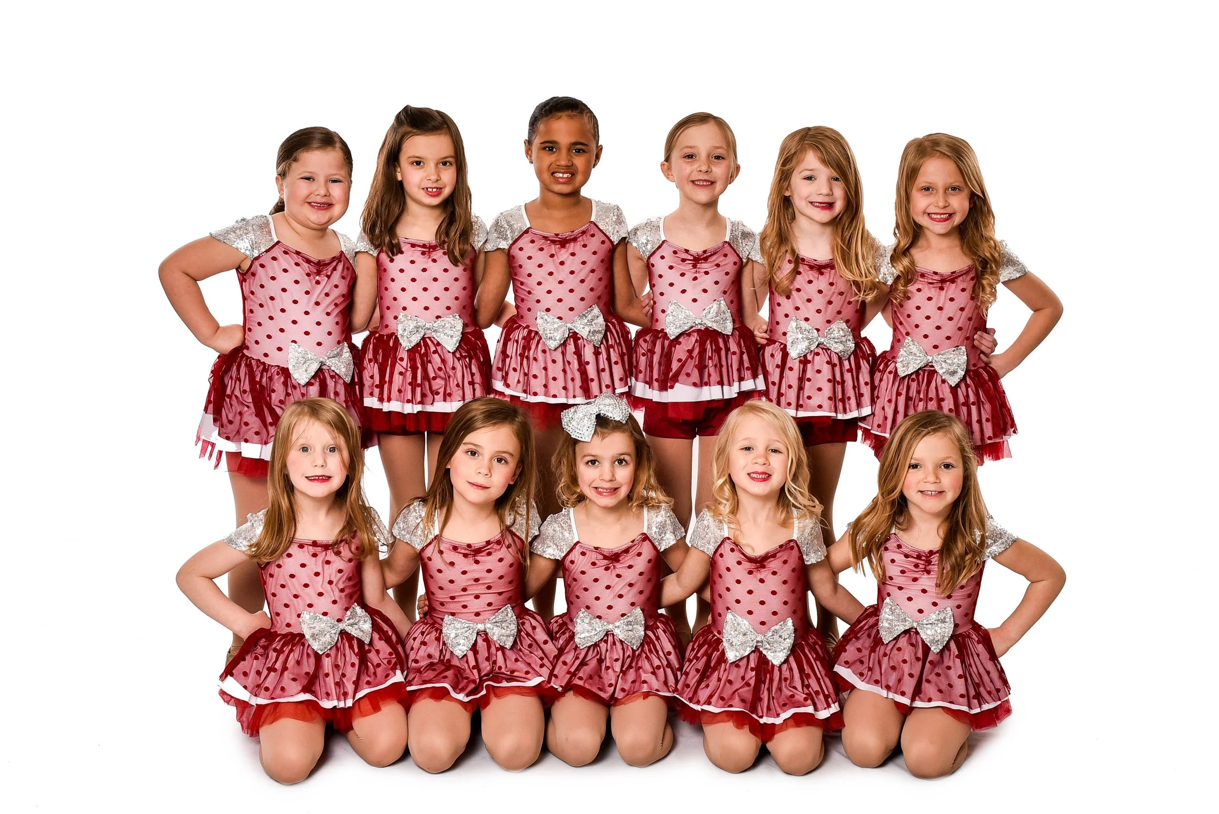 Group of 12 young girls in matching red and silver dance costumes posing for a photo against a white background.