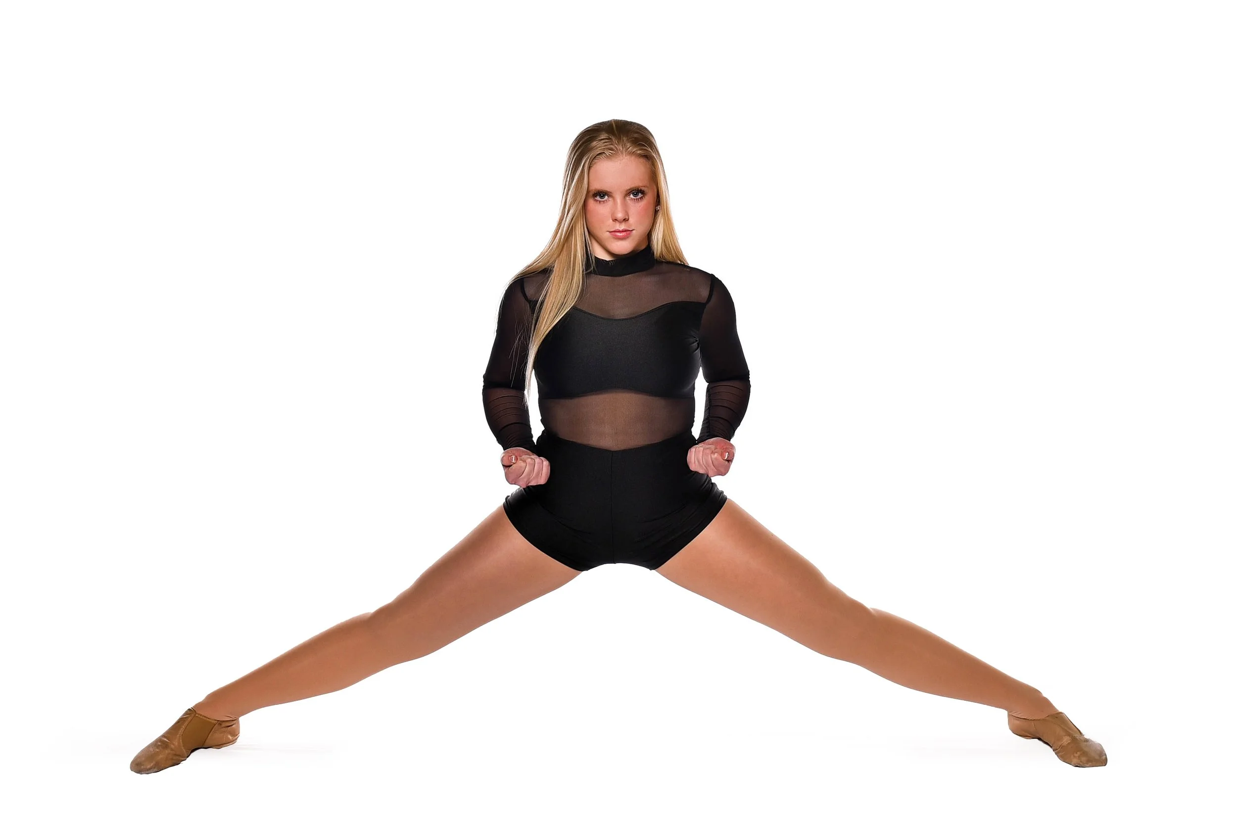 A female dancer in black attire stretching her legs wide apart on the ice rink.