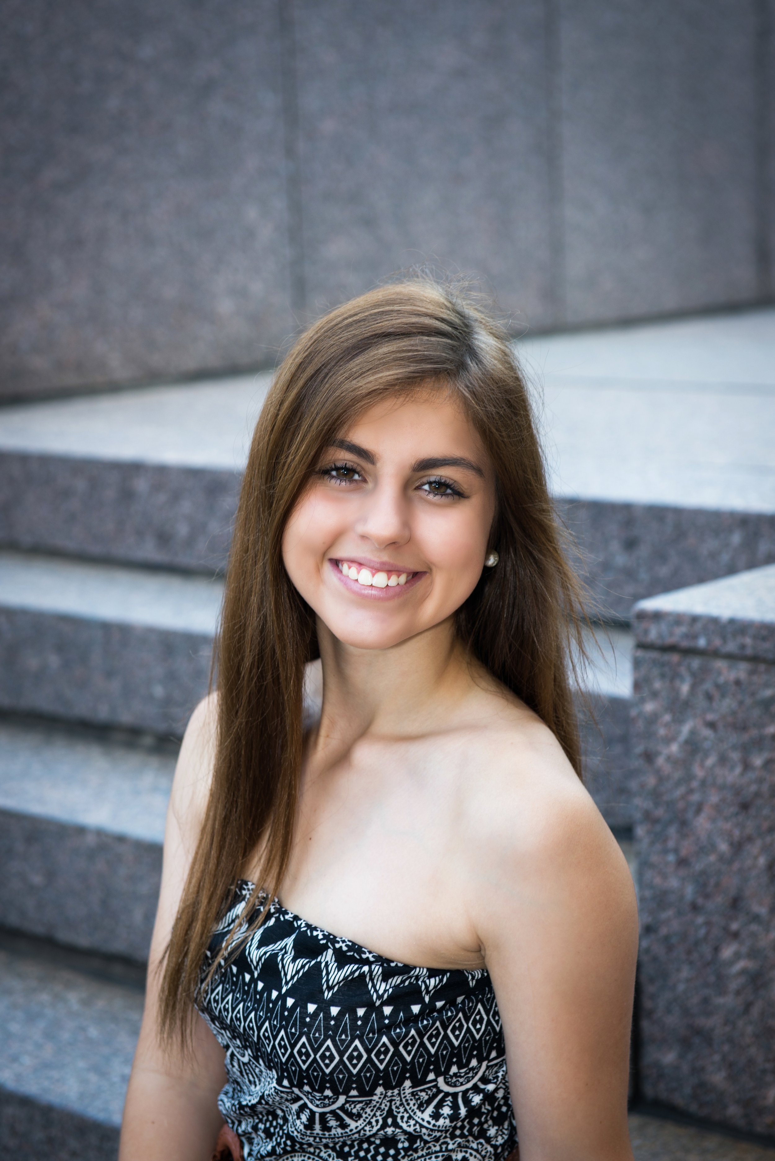 A young woman with long brown hair smiling in front of stone stairs.