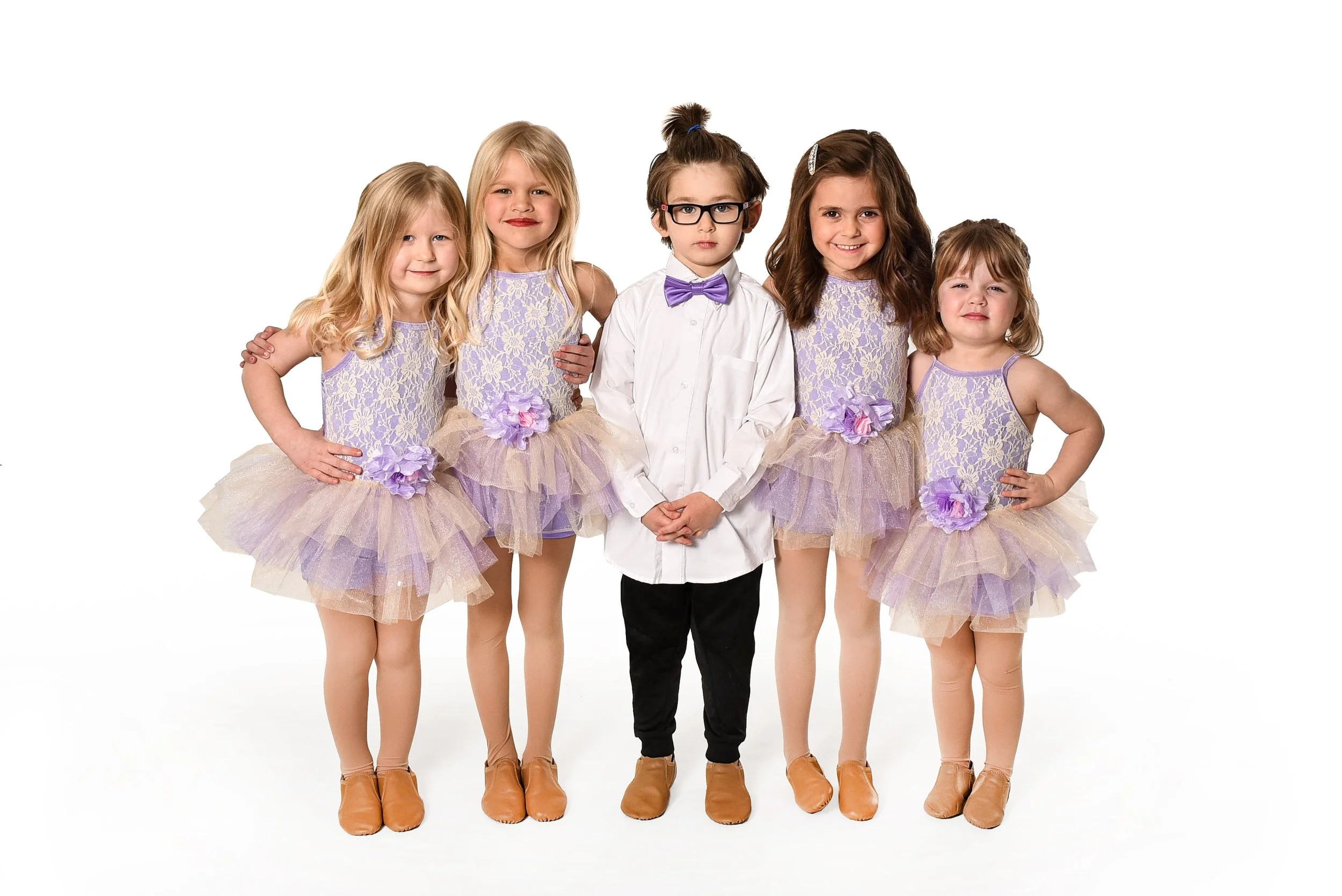 Five young girls and one young boy dressed in coordinated dance or costume outfits, standing side by side against a white background.
